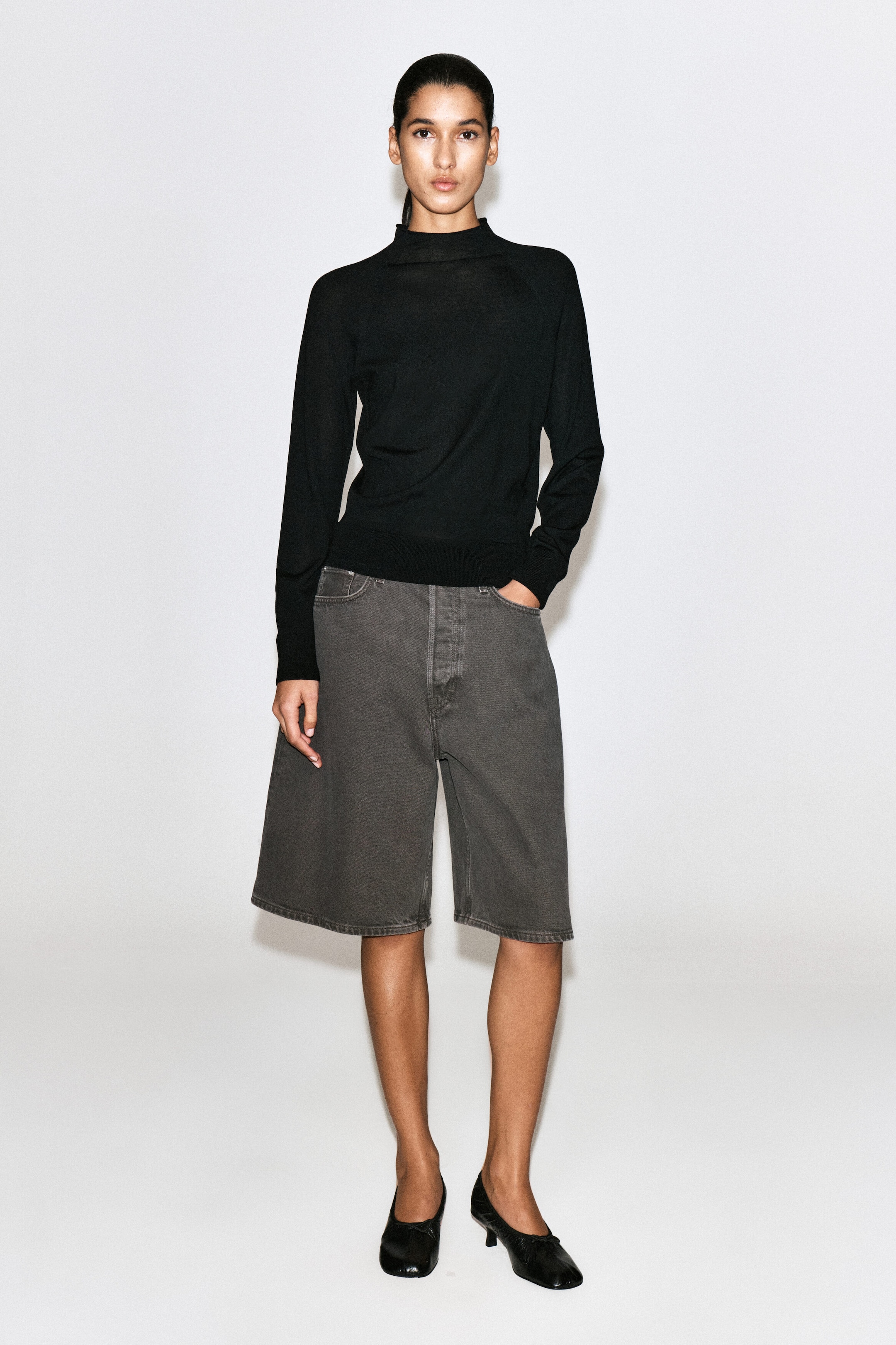 A pair of high-rise, longline denim shorts in a washed espresso-gray hue is shown from the front, featuring a wide-leg, knee-length silhouette with classic five-pocket detailing and tonal topstitching. A pair of high-rise, longline denim shorts in a washed espresso-gray hue is shown from the front, featuring a wide-leg, knee-length silhouette with classic five-pocket detailing and tonal topstitching.