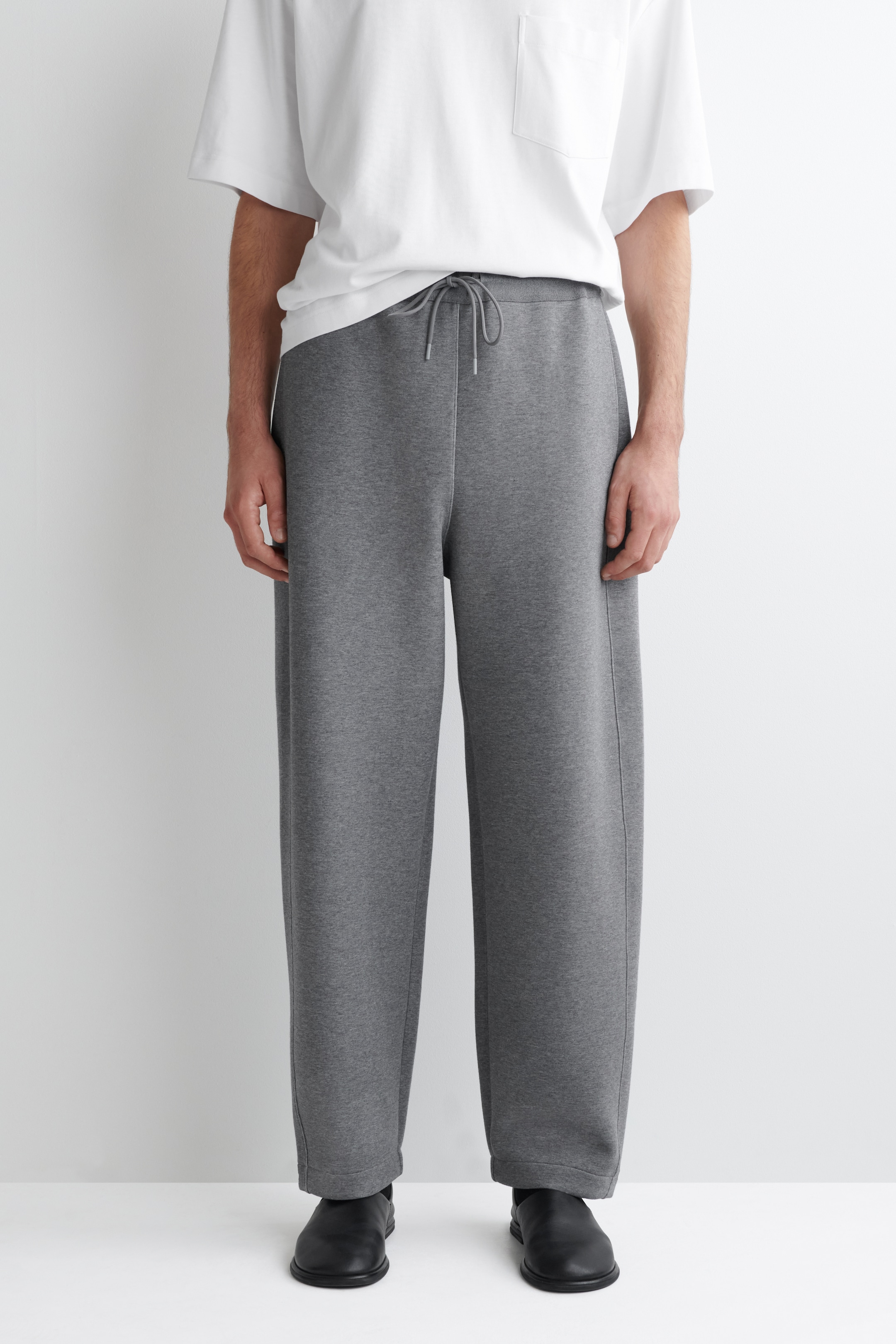 Größeres Bild ansehen: Graue Barrel-Leg-Jogger werden von vorne präsentiert, mit einer entspannten Passform und einem Kordelzugbund. Die Jogger sind mit weiten Beinen und vertikalen Nähten, die vorne verlaufen, gestaltet.