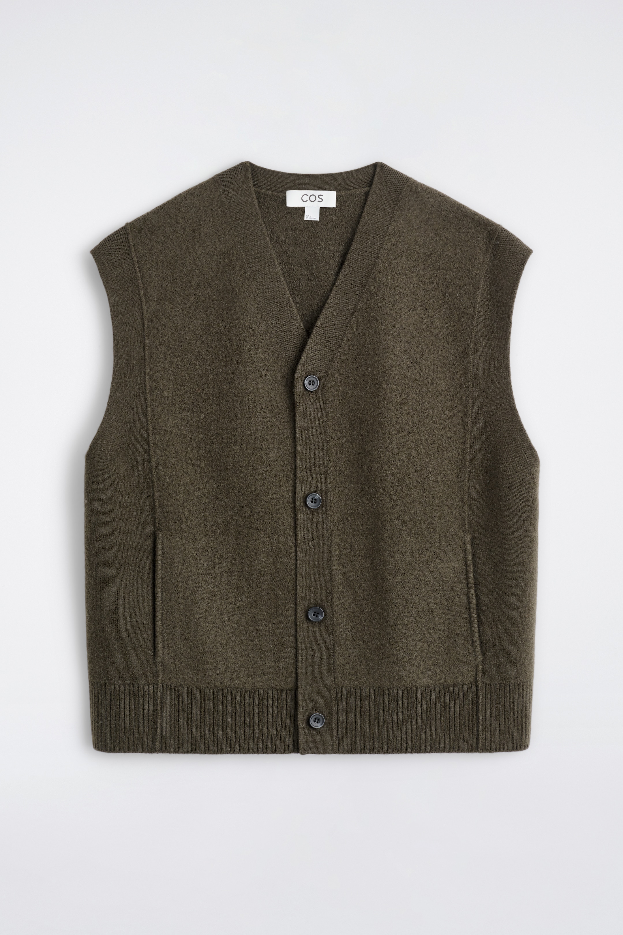 Agrandir l'image: Un gilet en laine bouillie vert olive foncé est présenté à l'avant, avec un col en V et une fermeture à boutons. Il est conçu avec des coutures apparentes, des poches frontales discrètes, ainsi que des panneaux latéraux et un ourlet côtelés.
