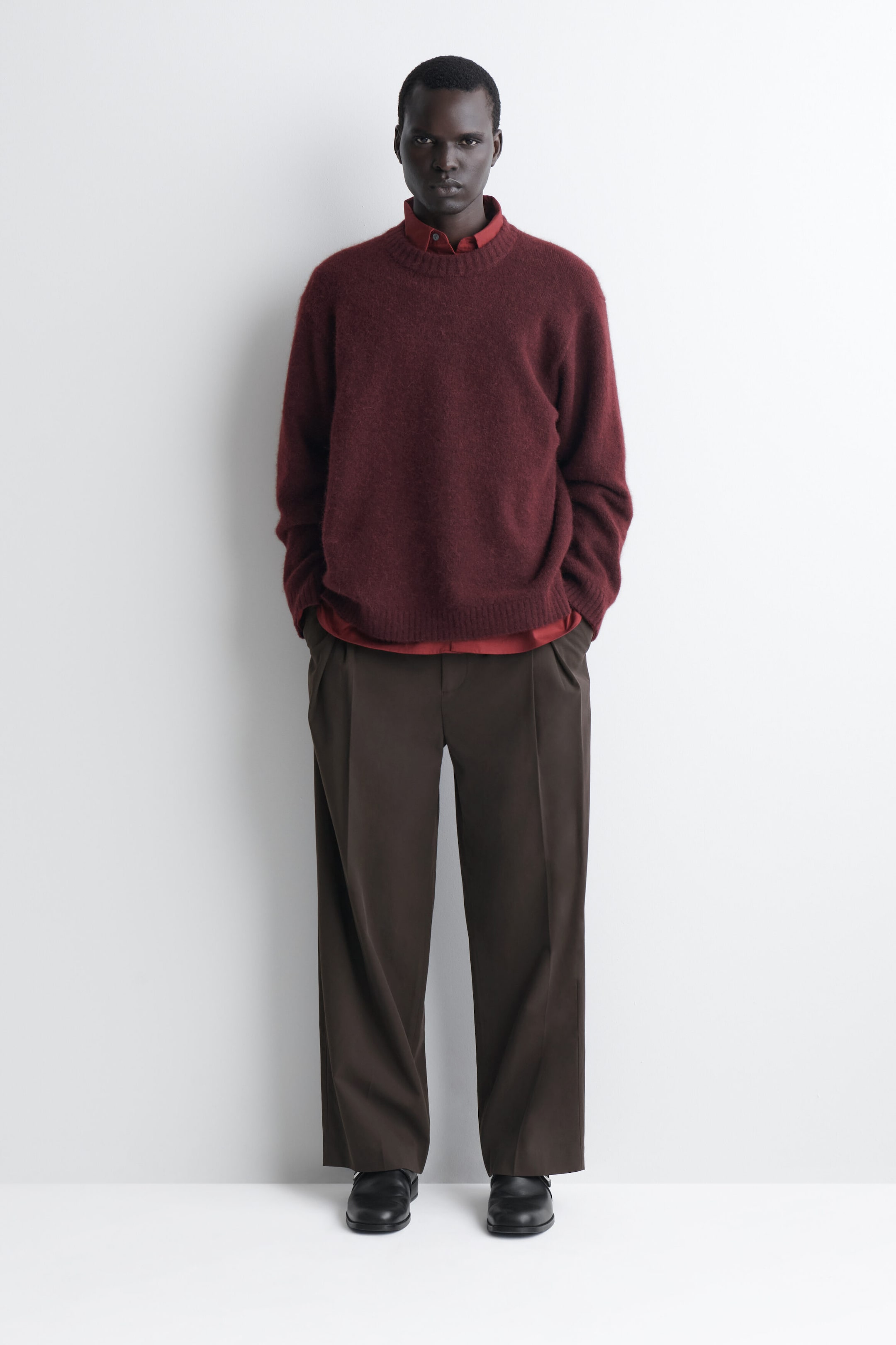 The oversized alpaca-blend crew-neck sweater is shown from the front on a model, showcasing a deep burgundy colour, a fuzzy texture, and a relaxed fit. It features a ribbed crew neck, ribbed cuffs, and a ribbed hem, and is styled over a red collared shirt that peeks out at the collar and hem. The oversized alpaca-blend crew-neck sweater is shown from the front on a model, showcasing a deep burgundy colour, a fuzzy texture, and a relaxed fit. It features a ribbed crew neck, ribbed cuffs, and a ribbed hem, and is styled over a red collared shirt that peeks out at the collar and hem.