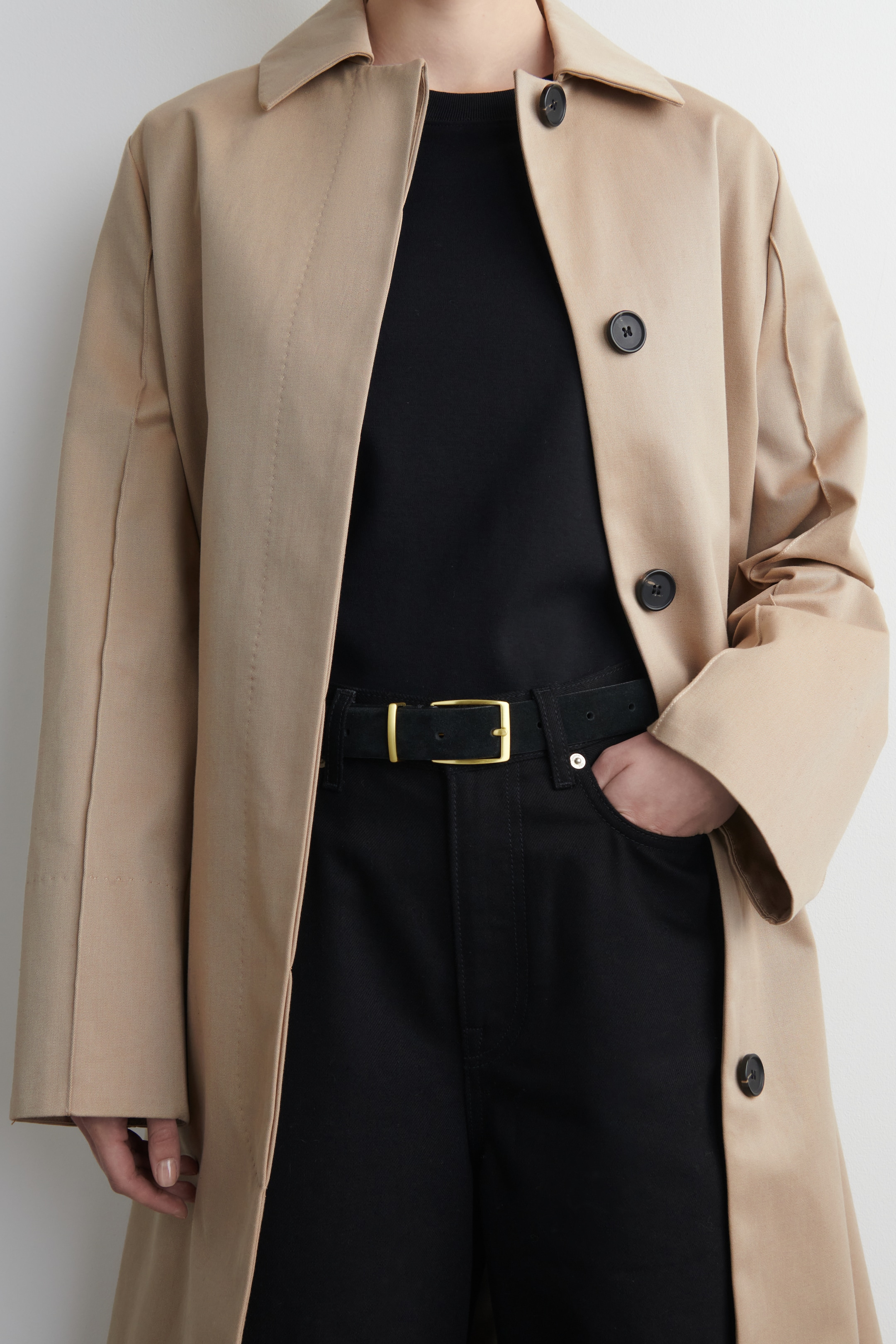 Agrandir l'image: Un trench-coat beige est présenté de face, porté ouvert sur un t-shirt noir et un pantalon noir. Il est doté de boutons ronds foncés le long de sa partie avant ouverte et d'un col à pointes classique.