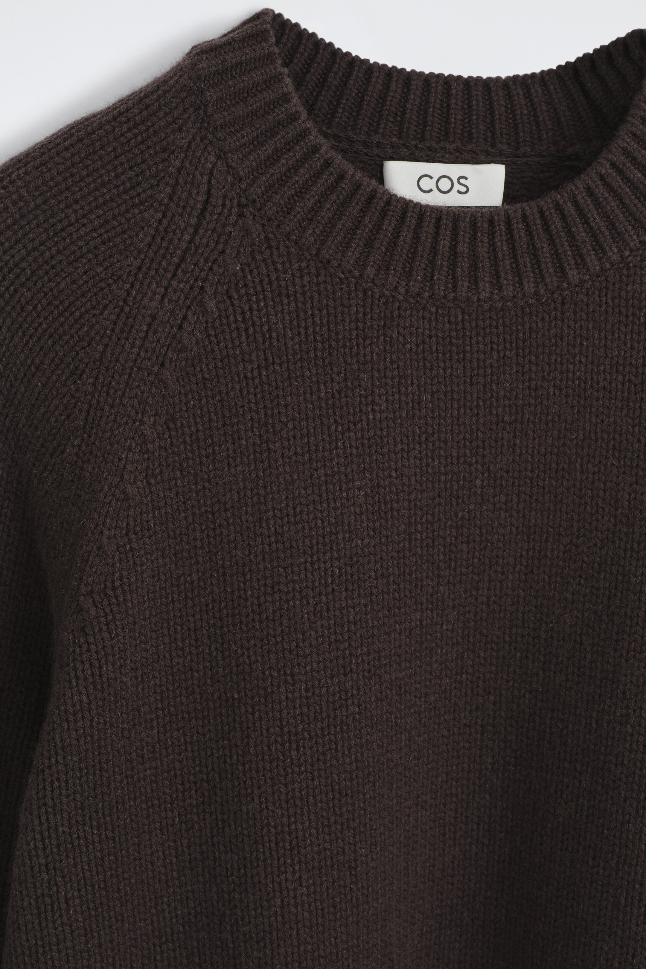 A chunky cashmere jumper in dark brown is displaying a ribbed crew neck and raglan shoulder seams in a close-up front view. The heavy-knit fabric is showcasing a soft, textured finish with a brand label visible inside the collar. A chunky cashmere jumper in dark brown is displaying a ribbed crew neck and raglan shoulder seams in a close-up front view. The heavy-knit fabric is showcasing a soft, textured finish with a brand label visible inside the collar.