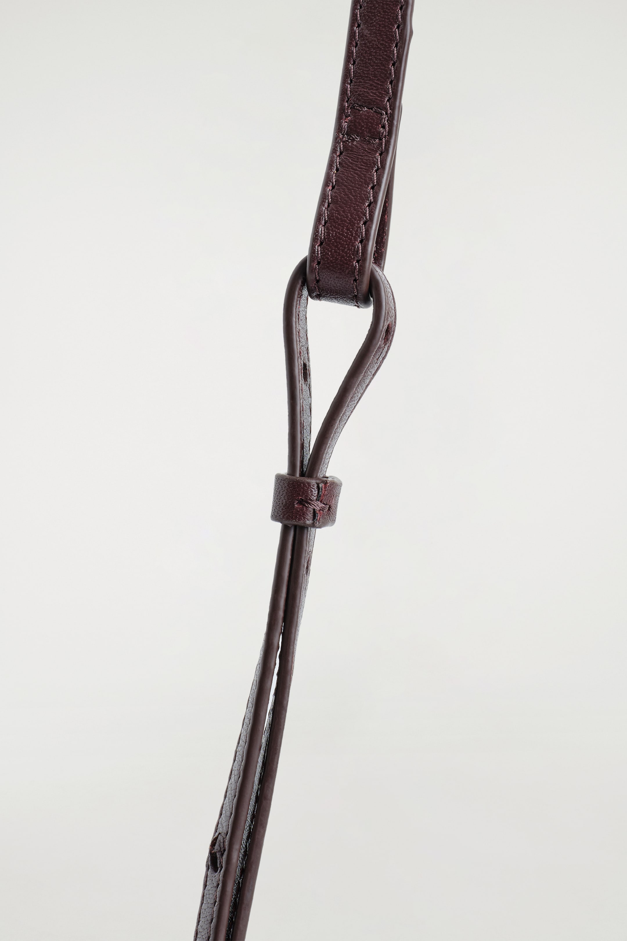 Agrandir l'image: TROVE CROSSBODY BAG - LEATHER est doté d'une sangle en cuir brun-rouge profond avec des surpiqûres visibles le long de ses bords. Une petite boucle en cuir sécurise la sangle, qui présente également des perforations pour l'ajustement de la taille.