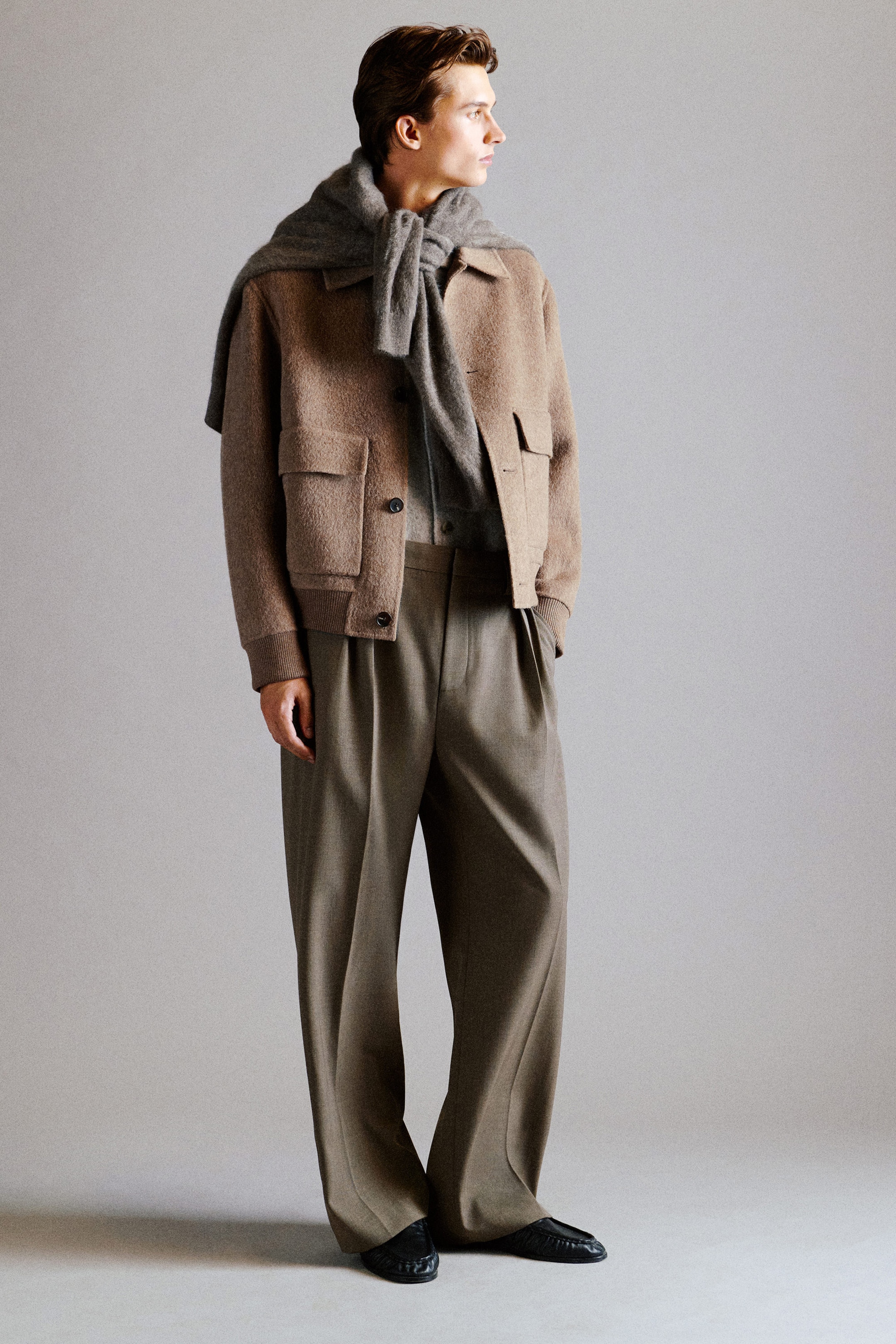 This beige wool-alpaca blend jacket is shown from the front on a model, featuring a relaxed fit, button-front closure, and large double-entry flap pockets. The textured jacket is finished with ribbed trims at the cuffs and hem, and is styled with a gray knit sweater draped over the shoulders and wide-leg pleated trousers. This beige wool-alpaca blend jacket is shown from the front on a model, featuring a relaxed fit, button-front closure, and large double-entry flap pockets. The textured jacket is finished with ribbed trims at the cuffs and hem, and is styled with a gray knit sweater draped over the shoulders and wide-leg pleated trousers.