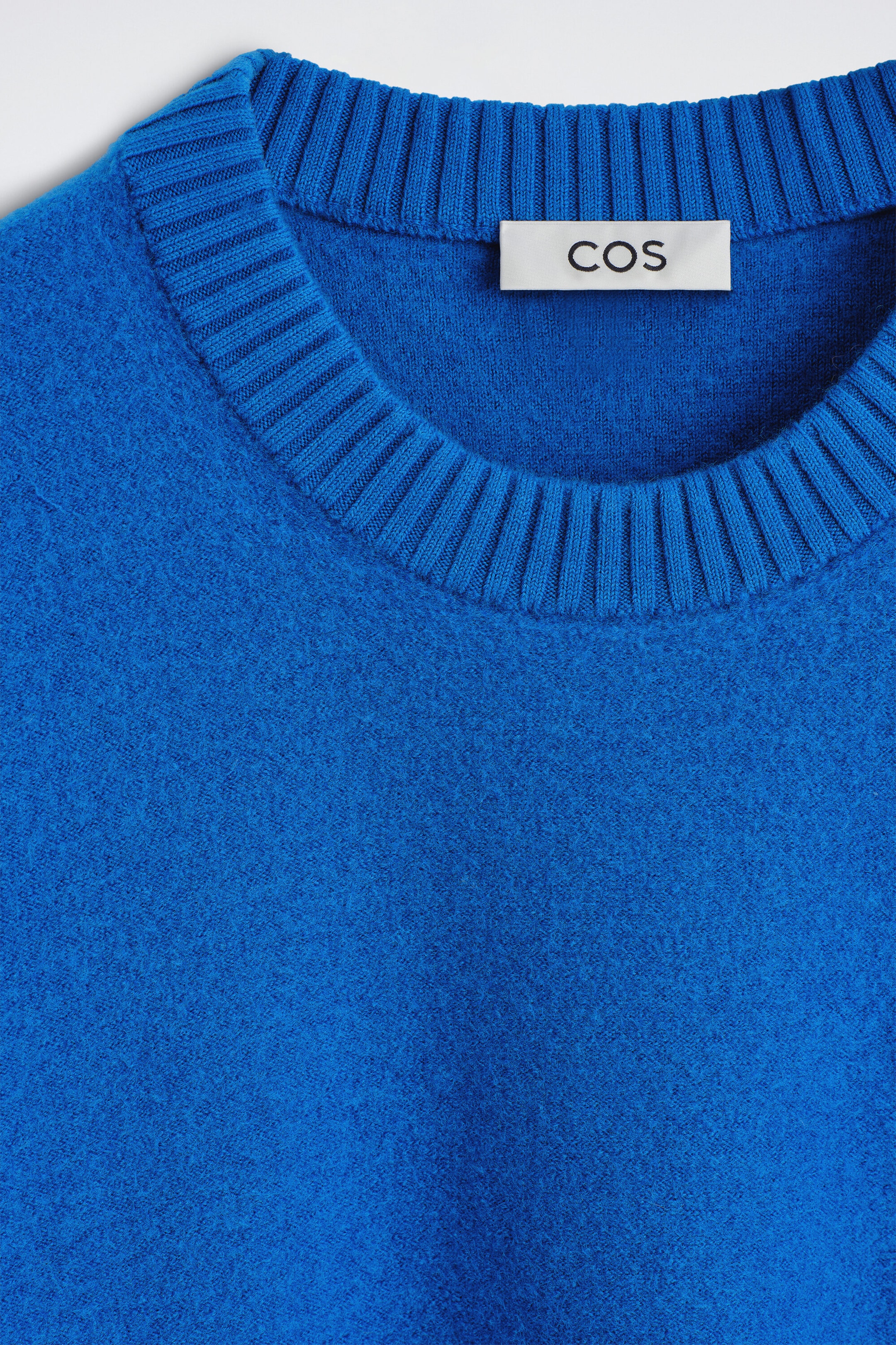 The BOILED MERINO WOOL CREW-NECK JUMPER is shown in a close-up, front-facing view, highlighting the textured, vibrant blue boiled wool fabric. The design features a thick ribbed crew-neck collar with a white brand label visible on the inside back. The BOILED MERINO WOOL CREW-NECK JUMPER is shown in a close-up, front-facing view, highlighting the textured, vibrant blue boiled wool fabric. The design features a thick ribbed crew-neck collar with a white brand label visible on the inside back.