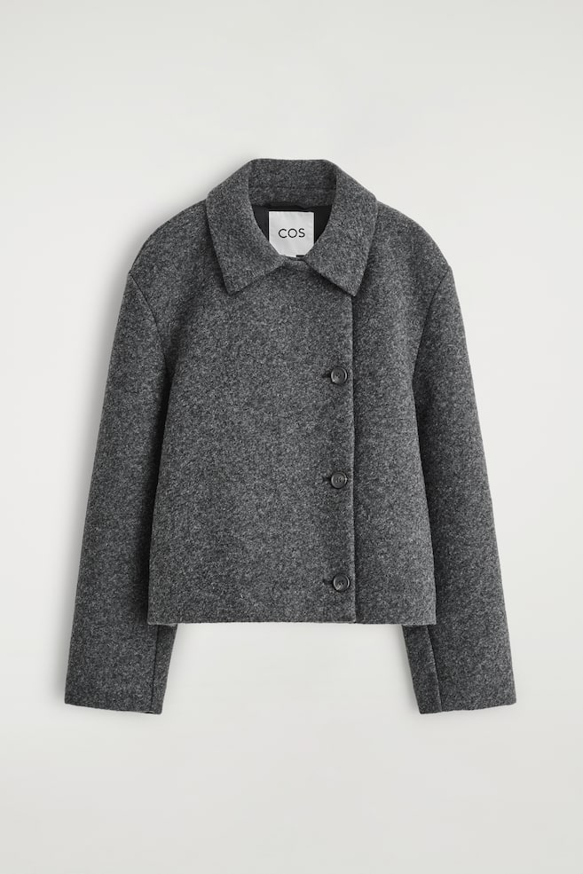 A dark grey, mottled jacket is displaying from the FRONT. It is featuring a cropped, structured silhouette, a classic pointed collar, and softly rounded shoulders, with three dark, round buttons fastening the jacket off-centre. - 1