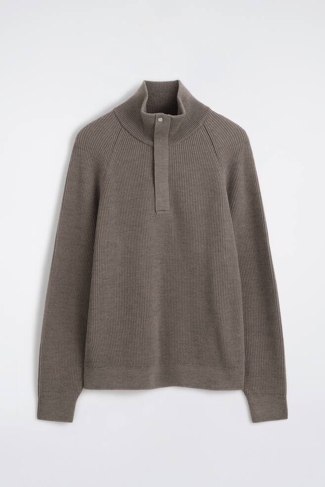 Un jersey de lana de media cremallera y canalÃ© aparece de frente, con una textura de punto acanalado en gris topo, mangas raglÃ¡n y cuello alto. El jersey presenta una tapeta frontal cubierta con un Ãºnico botÃ³n de presiÃ³n visible en la parte superior, rematada con puÃ±os de canalÃ© fino y bajo a juego. - 1