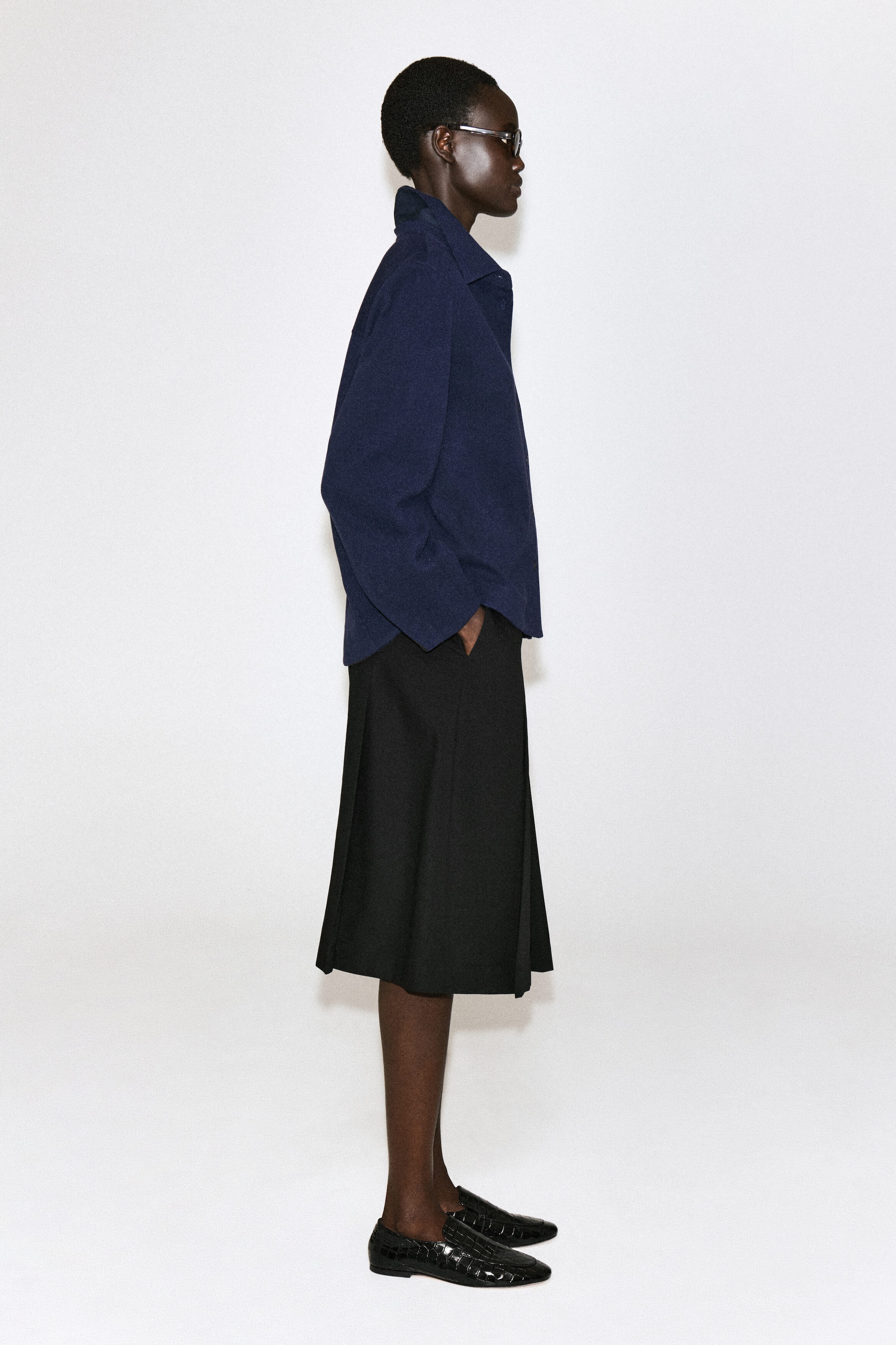 A navy corduroy jersey shirt is shown in side profile facing right, featuring a relaxed fit, pointed collar, and long sleeves. The shirt is worn untucked over a black skirt, highlighting its soft structure and casual drape. A navy corduroy jersey shirt is shown in side profile facing right, featuring a relaxed fit, pointed collar, and long sleeves. The shirt is worn untucked over a black skirt, highlighting its soft structure and casual drape.