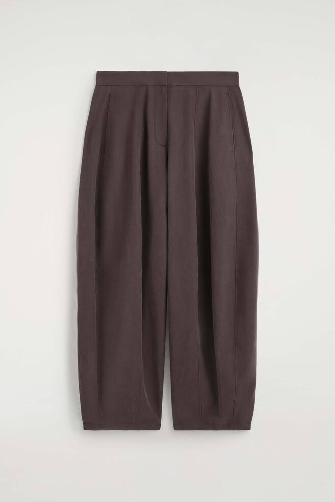 These dark brown toggle-hem wide-leg trousers are shown from the front, showcasing a high-waisted silhouette with a clean waistband and a concealed front fastening. The design features deep front pleats and side pockets, creating a voluminous, structured shape that tapers slightly towards the hem. - 1