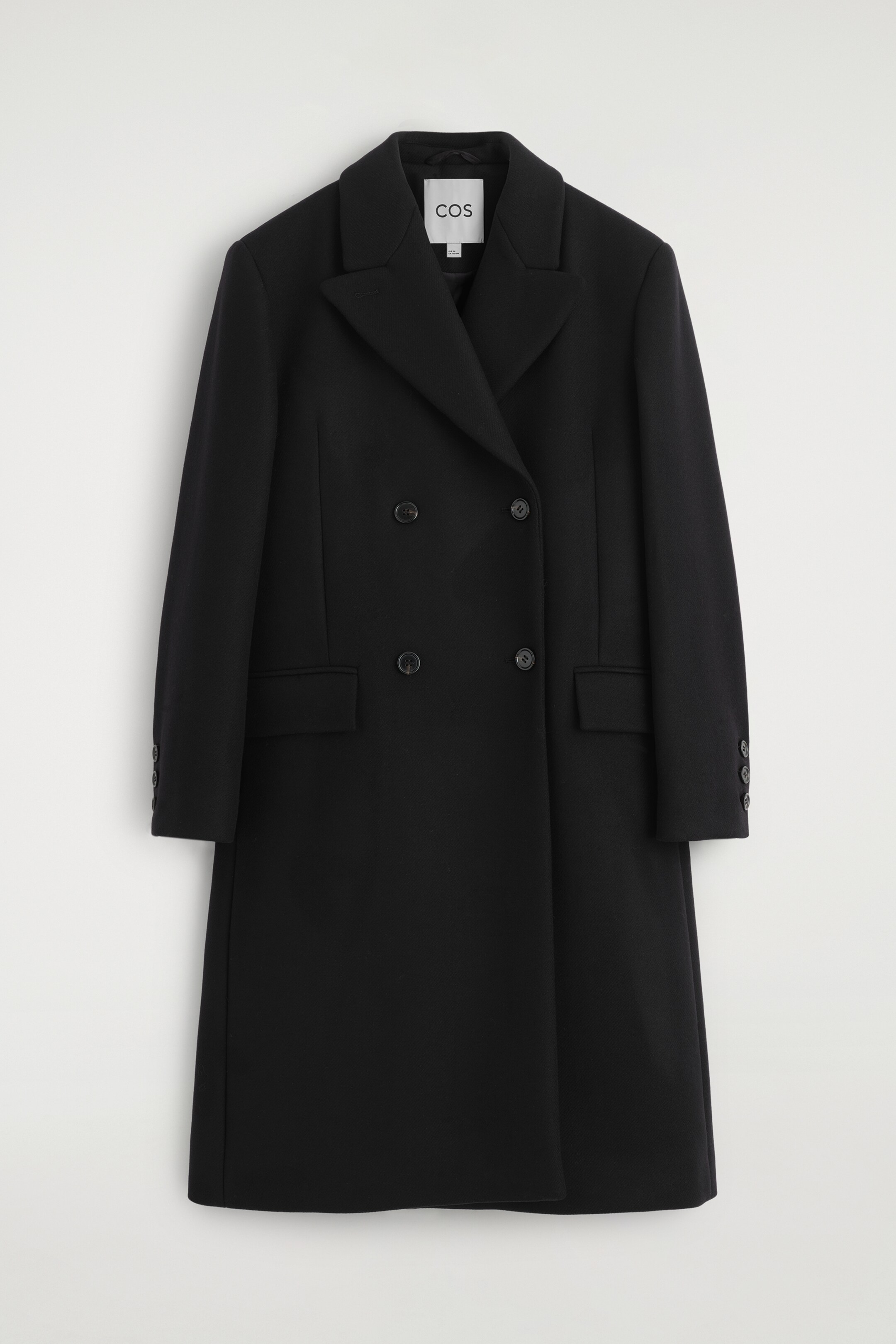 Ingrandisci l'immagine: Un lungo cappotto nero doppiopetto è presentato FRONT, con revers a lancia e una chiusura a quattro bottoni. Due tasche con patta sono visibili sui fianchi, e su ogni polsino ci sono tre bottoni più piccoli.