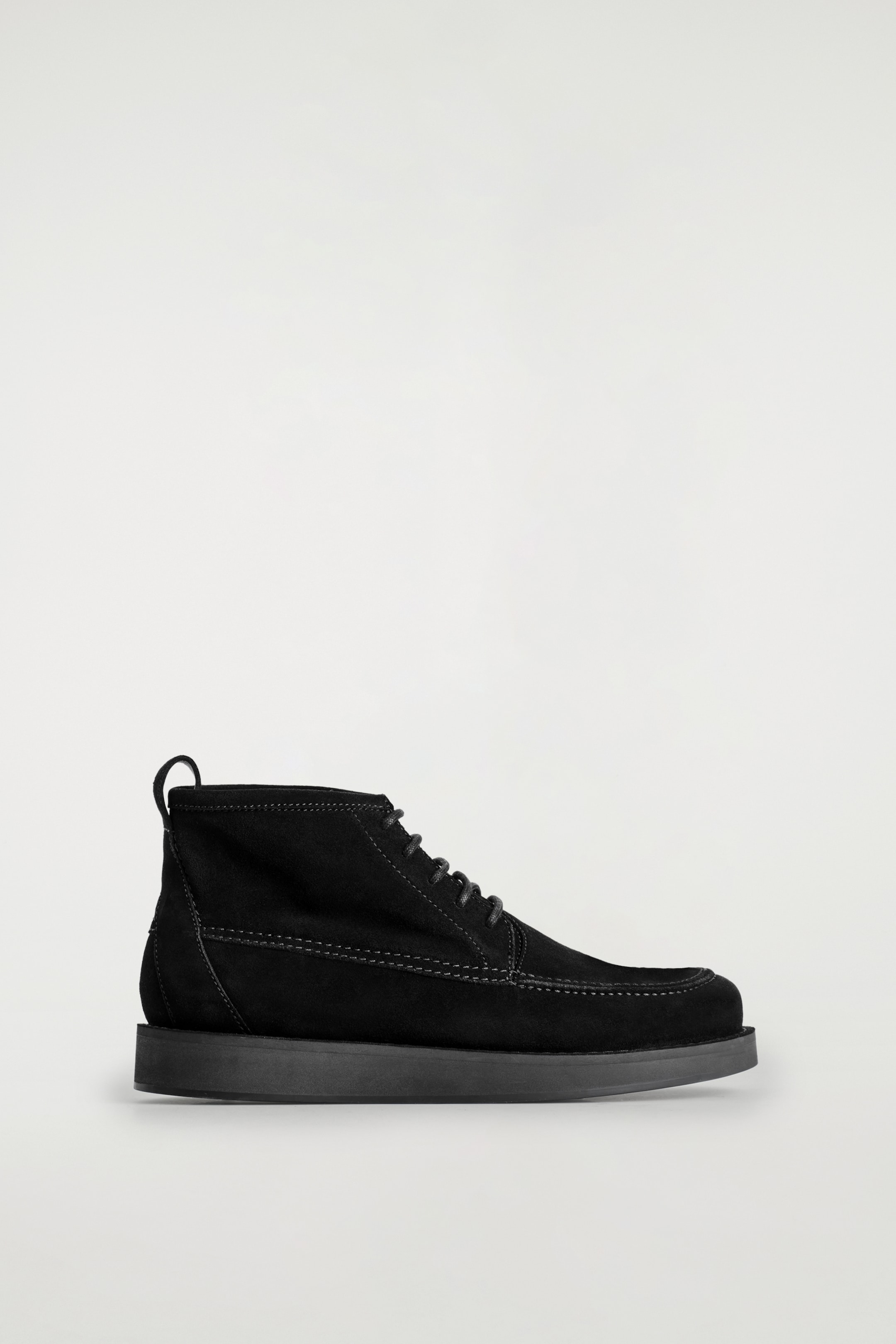 Visualizza immagine più grande: Un desert boot in camoscio nero spazzolato è rivolto a destra, caratterizzato da una chiusura con lacci in cera grigio scuro, cuciture a contrasto grigio chiaro lungo la punta moc e i pannelli laterali, e una spessa suola nera tonale.