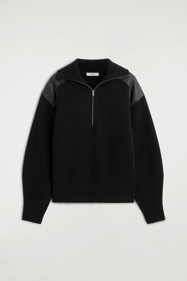 The leather-patch merino wool zip-up jumper is shown from the front, featuring a half-zip fastening with a silver metal zip and an open ribbed collar. It displays smooth black leather panels on the shoulders, long sleeves with ribbed cuffs, and a ribbed hem. - 1