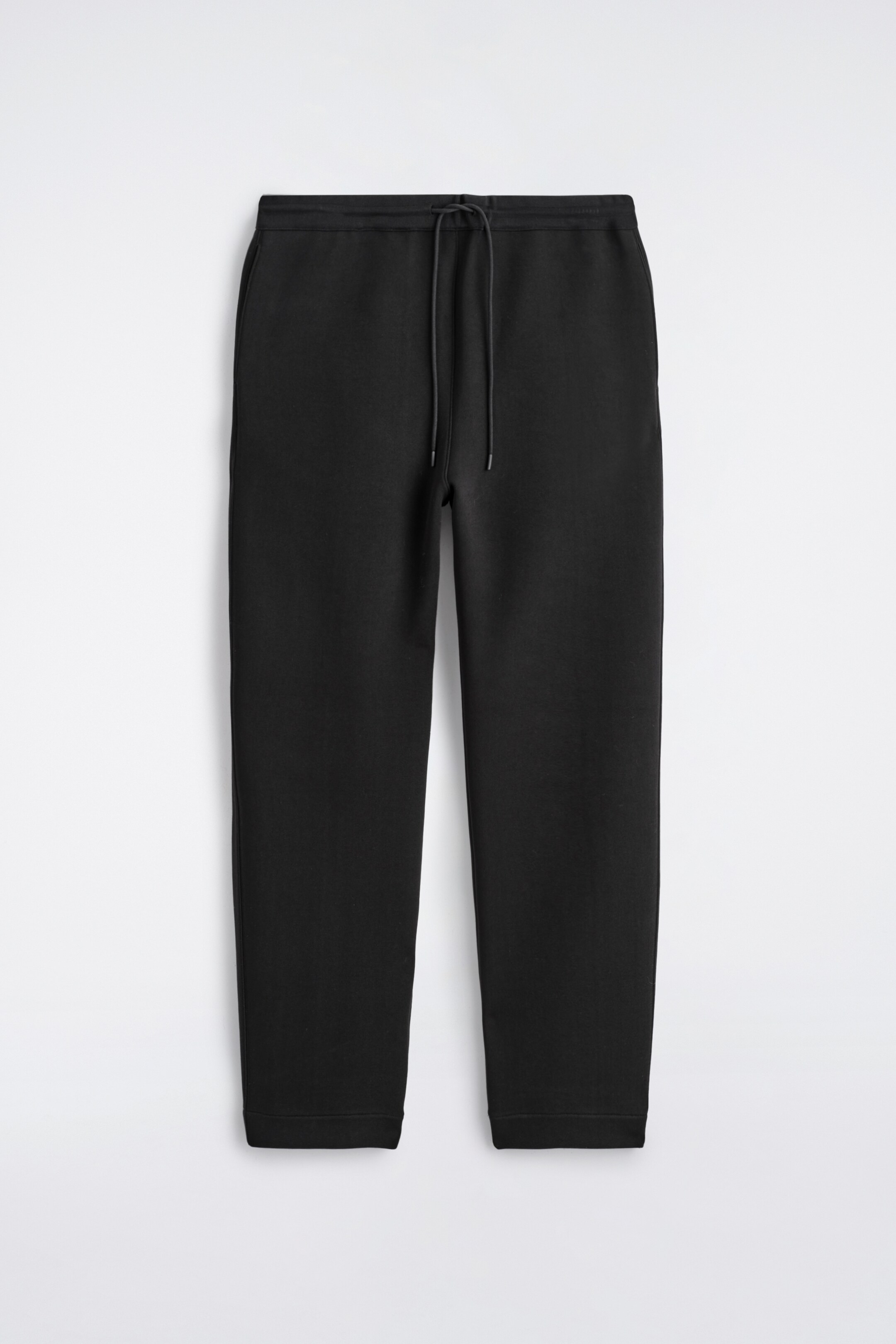 Agrandir l'image: Une paire de joggeurs à jambes larges noirs est présentée de face. Ils présentent une coupe décontractée, une ceinture à cordon de serrage visible et des poches latérales, avec des ourlets simples aux chevilles.