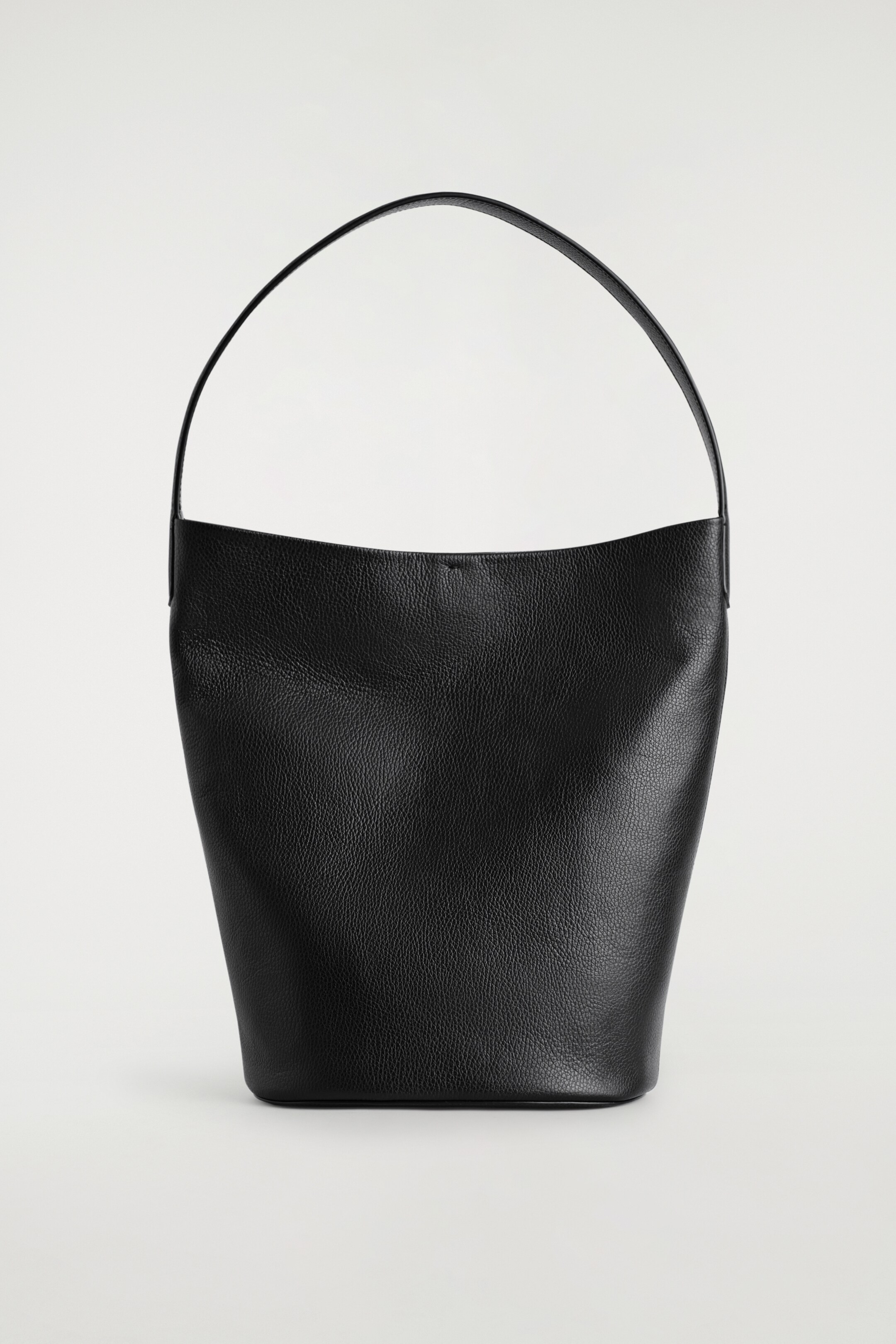 Ver imagem maior: Uma mala de couro preto está a ser apresentada de FRENTE, com uma silhueta descontraída em estilo de balde. É feita de couro texturizado, com uma única alça delgada arqueando-se acima das suas bordas superiores suavemente curvas.