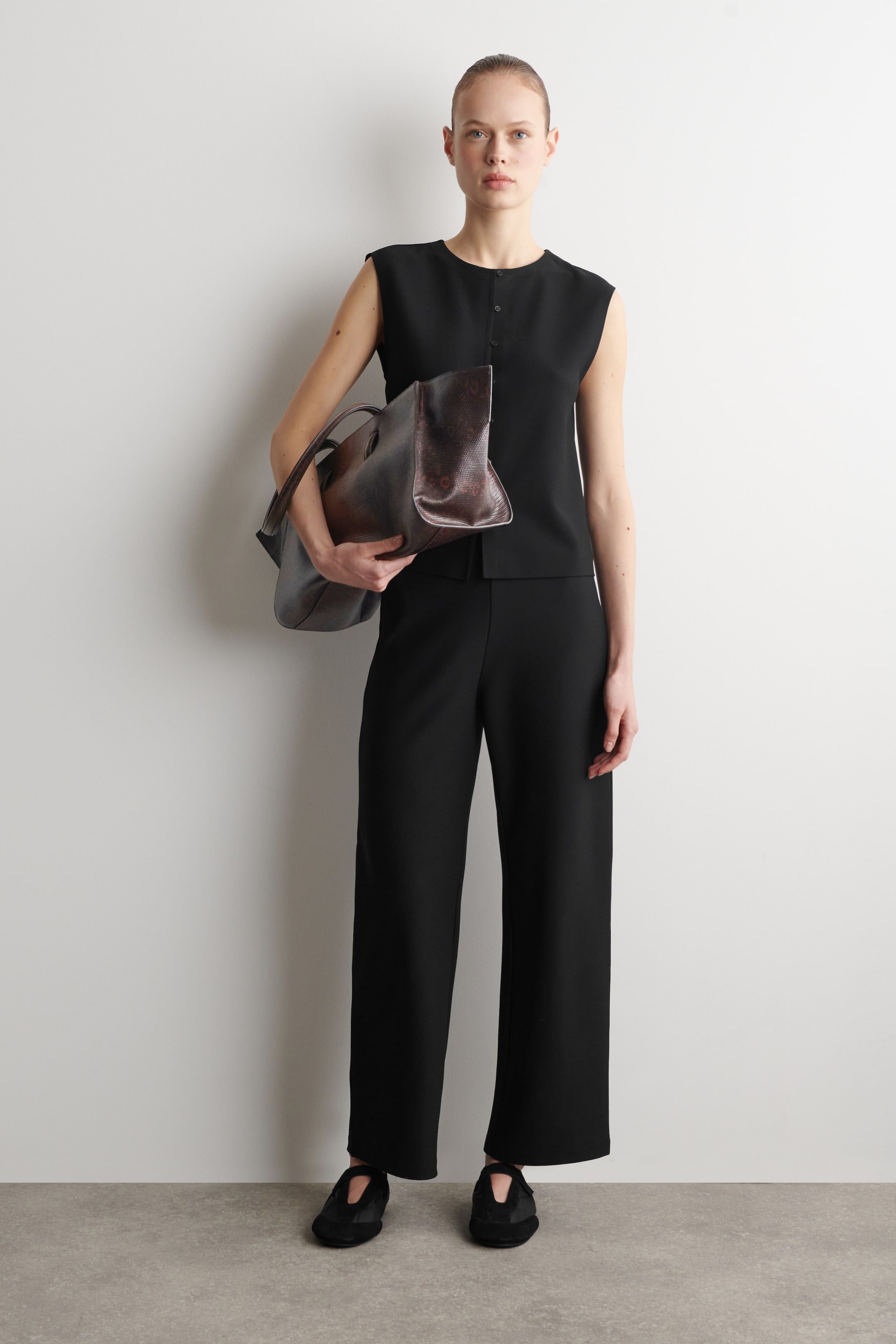 Größeres Bild anzeigen: Eine große dunkelbraune Handtasche wird gehalten, mit einer strukturierten Oberfläche und zwei oberen Griffen. Die Tasche zeigt ihre Vorderseite und die offene Oberseite.