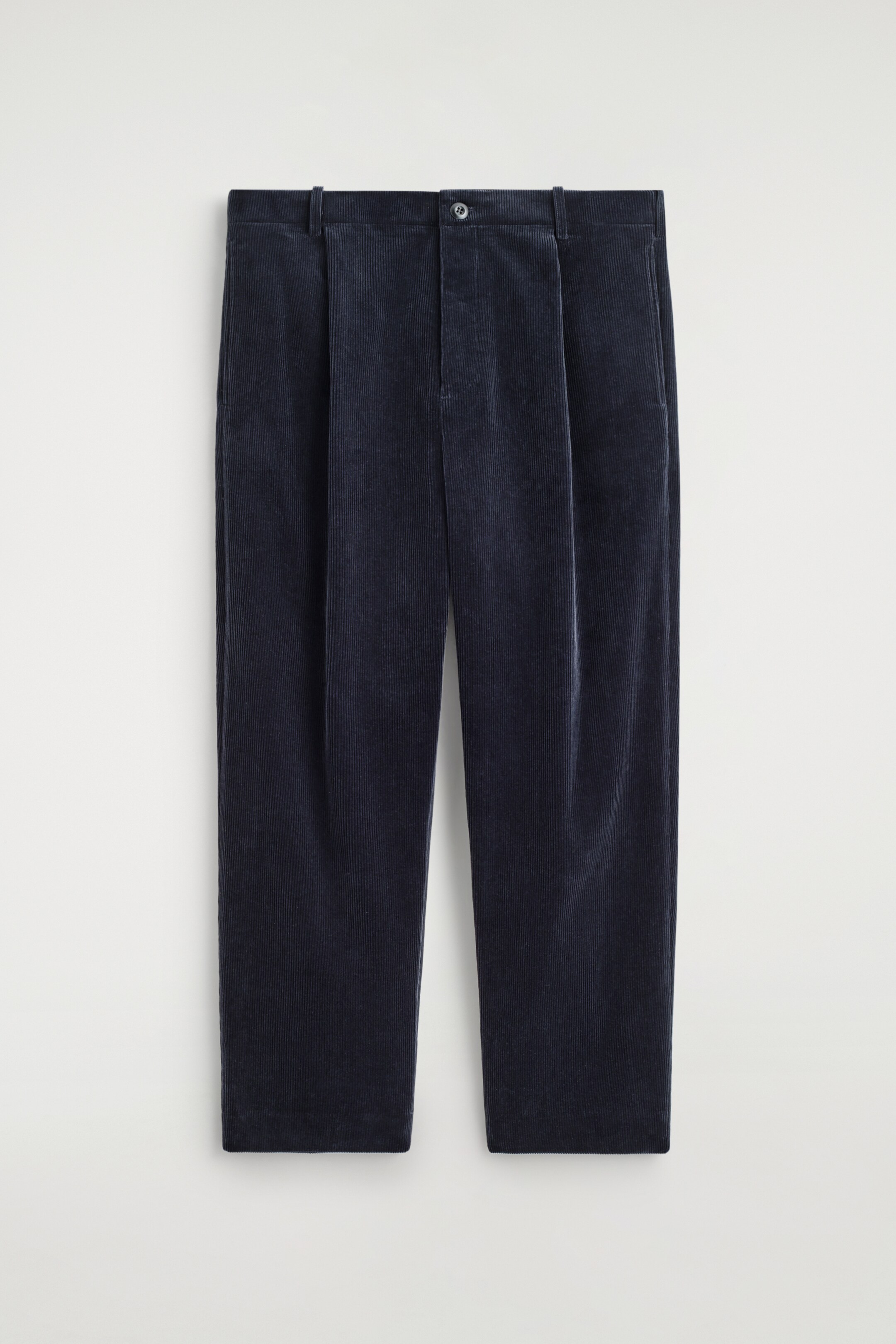 Agrandir l'image: Un pantalon en velours côtelé bleu foncé est présenté de face, avec une fermeture à bouton et braguette à la taille, des passants de ceinture et des plis doubles de chaque côté. Les poches dans les coutures latérales sont également visibles.