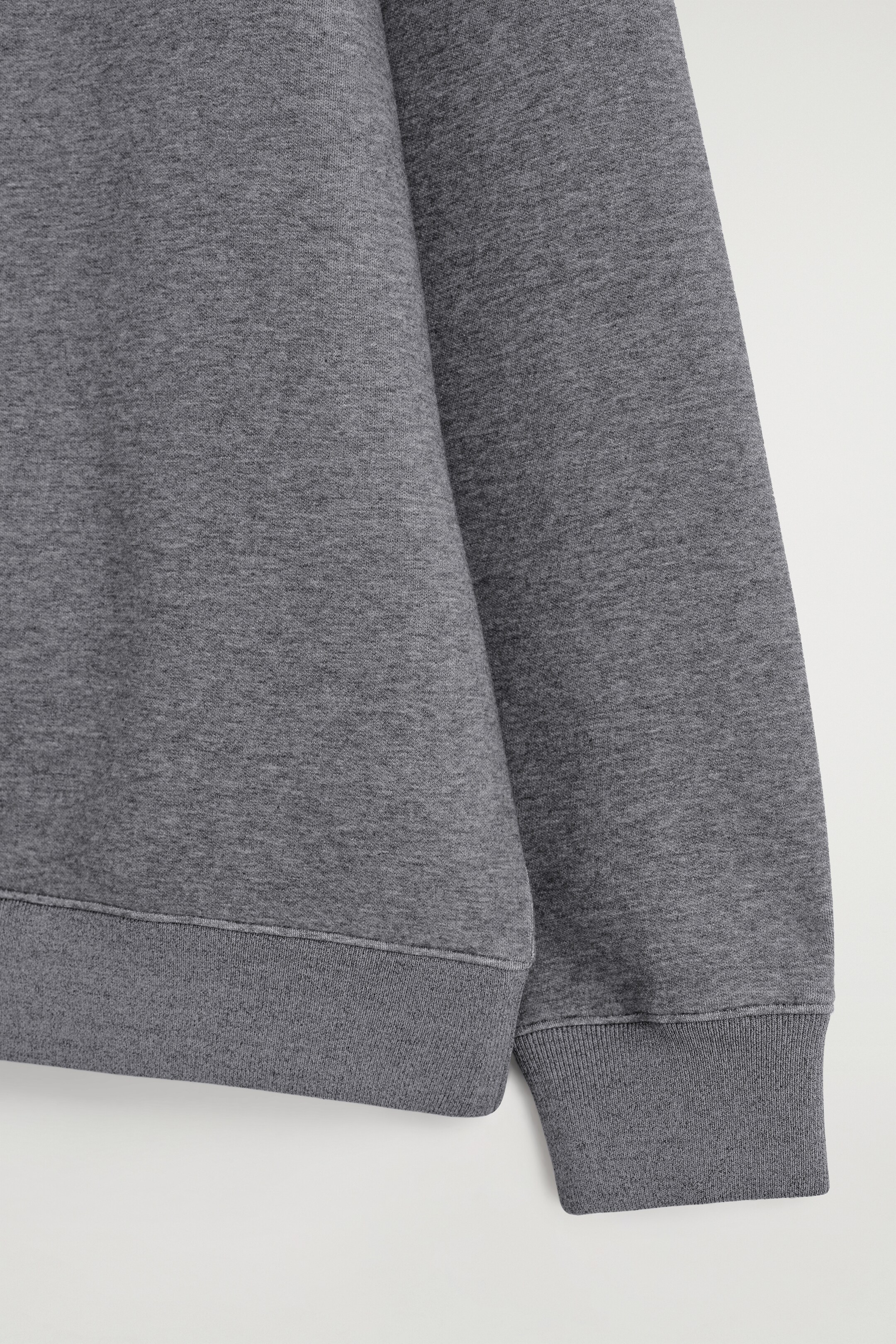 Ver imagem maior: Uma camisola cinzenta exibe um corte descontraído e uma textura mesclada subtil. Apresenta acabamentos finamente canelados na bainha e no punho.