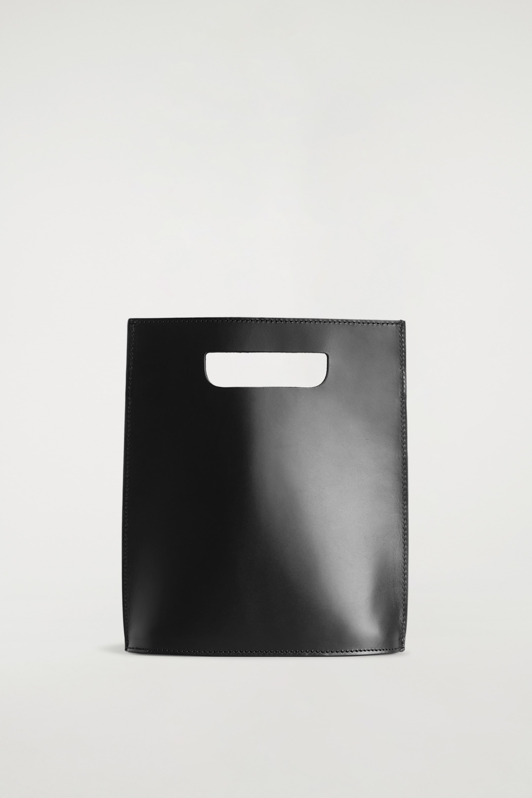 Visualizza immagine più grande: Una borsa Folio in pelle nera è presentata frontalmente, caratterizzata da un corpo rettangolare sottile e strutturato. È progettata con un manico ritagliato orizzontalmente al centro nella parte superiore e cuciture tonali visibili lungo i bordi.