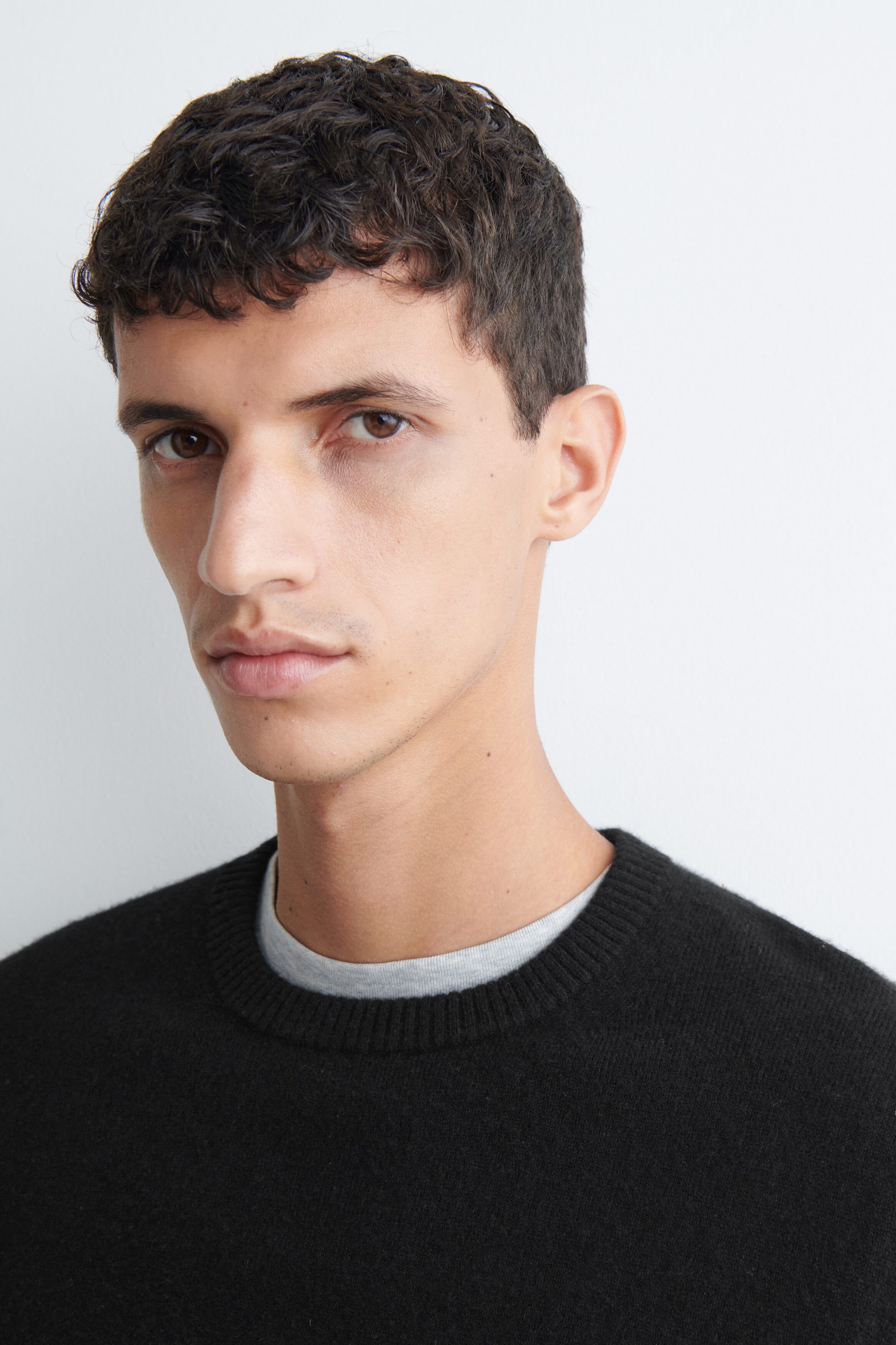 Das Modell trägt einen schwarzen Rundhalspullover, kombiniert mit einem hellgrauen T-Shirt. Der Pullover verfügt über eine weiche Strickstruktur und einen gerippten Ausschnitt. Das Modell trägt einen schwarzen Rundhalspullover, kombiniert mit einem hellgrauen T-Shirt. Der Pullover verfügt über eine weiche Strickstruktur und einen gerippten Ausschnitt.