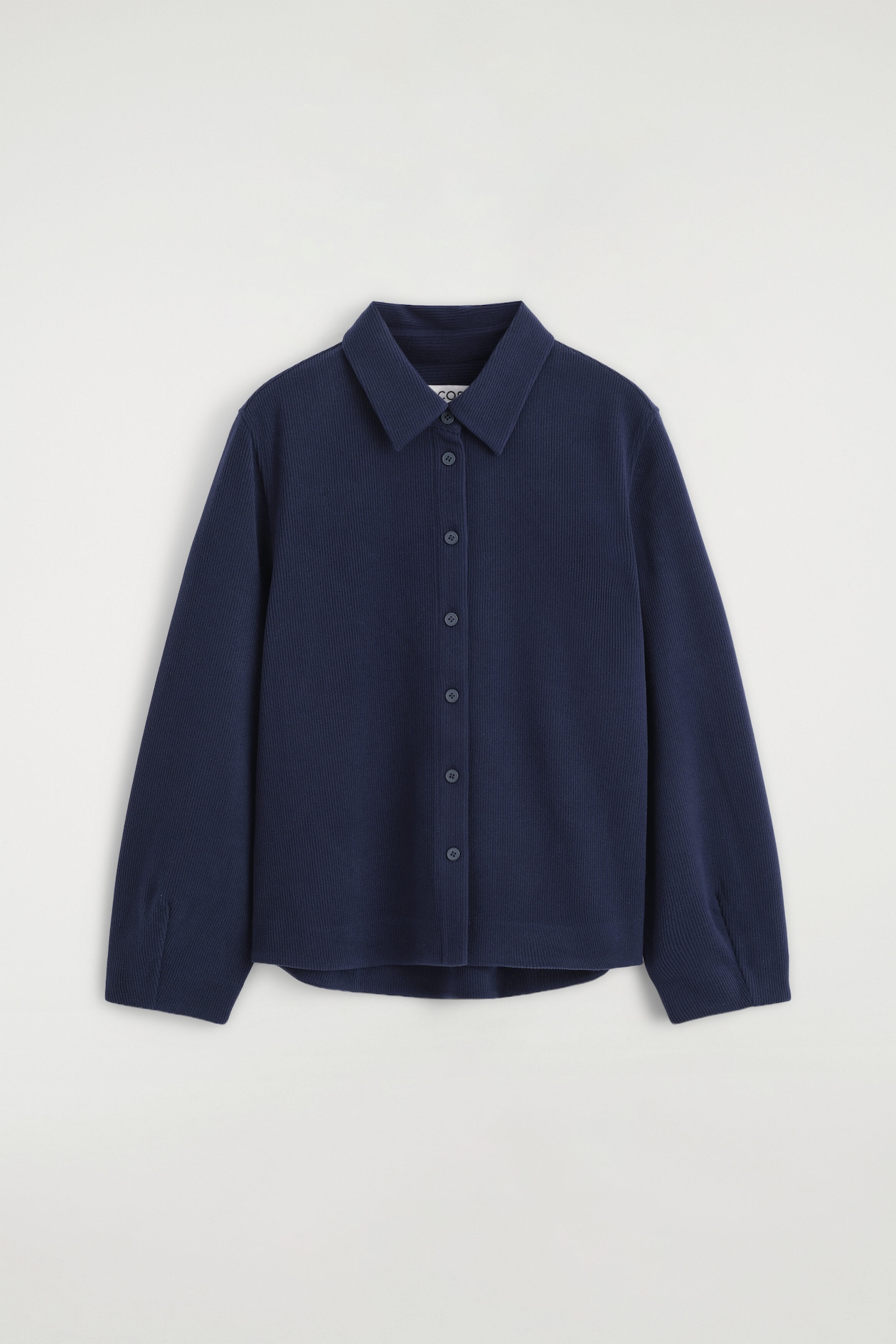 A navy blue corduroy-jersey shirt is shown from the front, featuring a classic point collar, a button-down front with matching buttons, and long sleeves with a textured, ribbed finish.