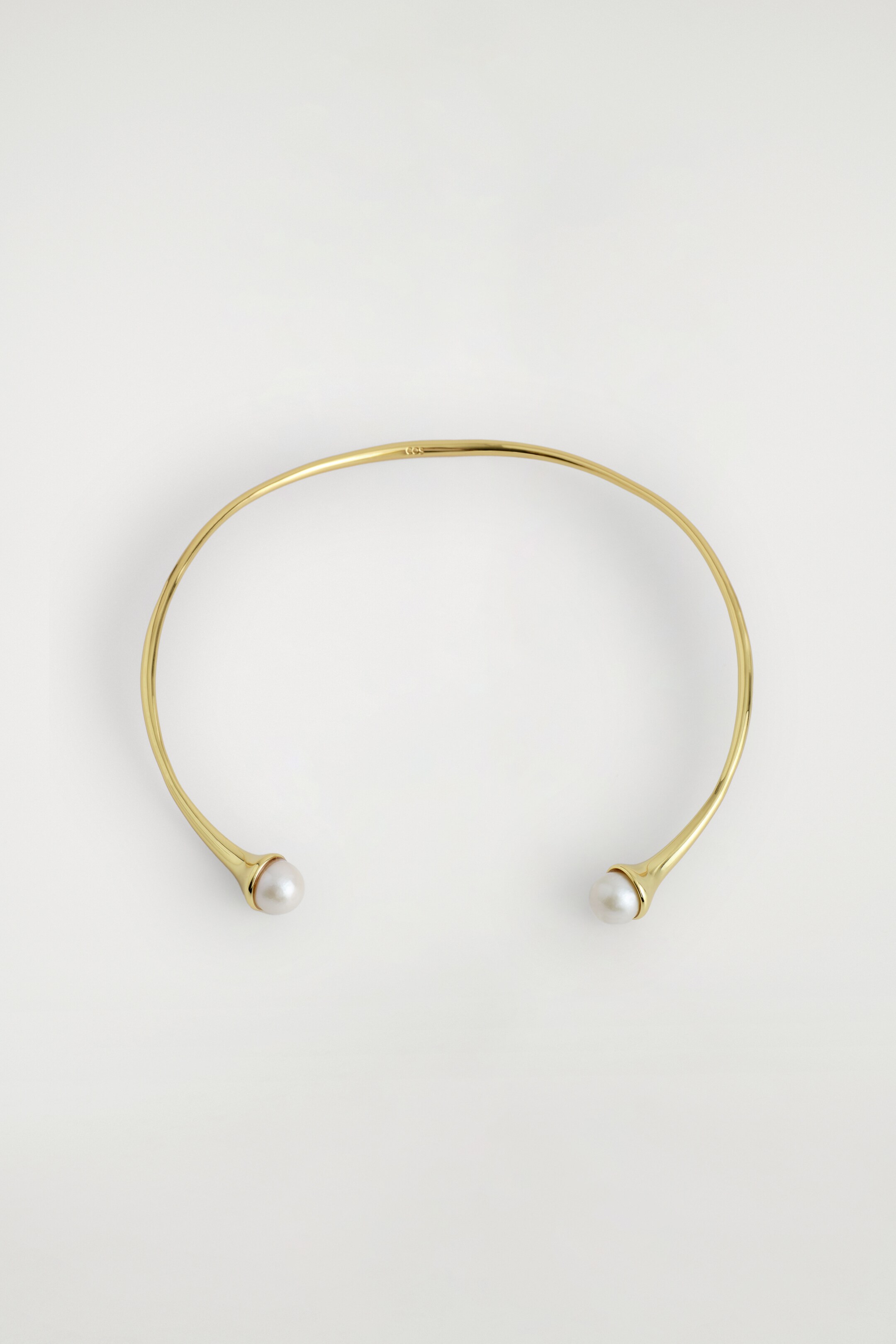 Ver imagem maior: Um colar tipo gargantilha dourado apresenta-se de um ângulo SUPERIOR, ostentando uma silhueta curva e aberta. É adornado com uma pérola de água doce esférica em cada extremidade.