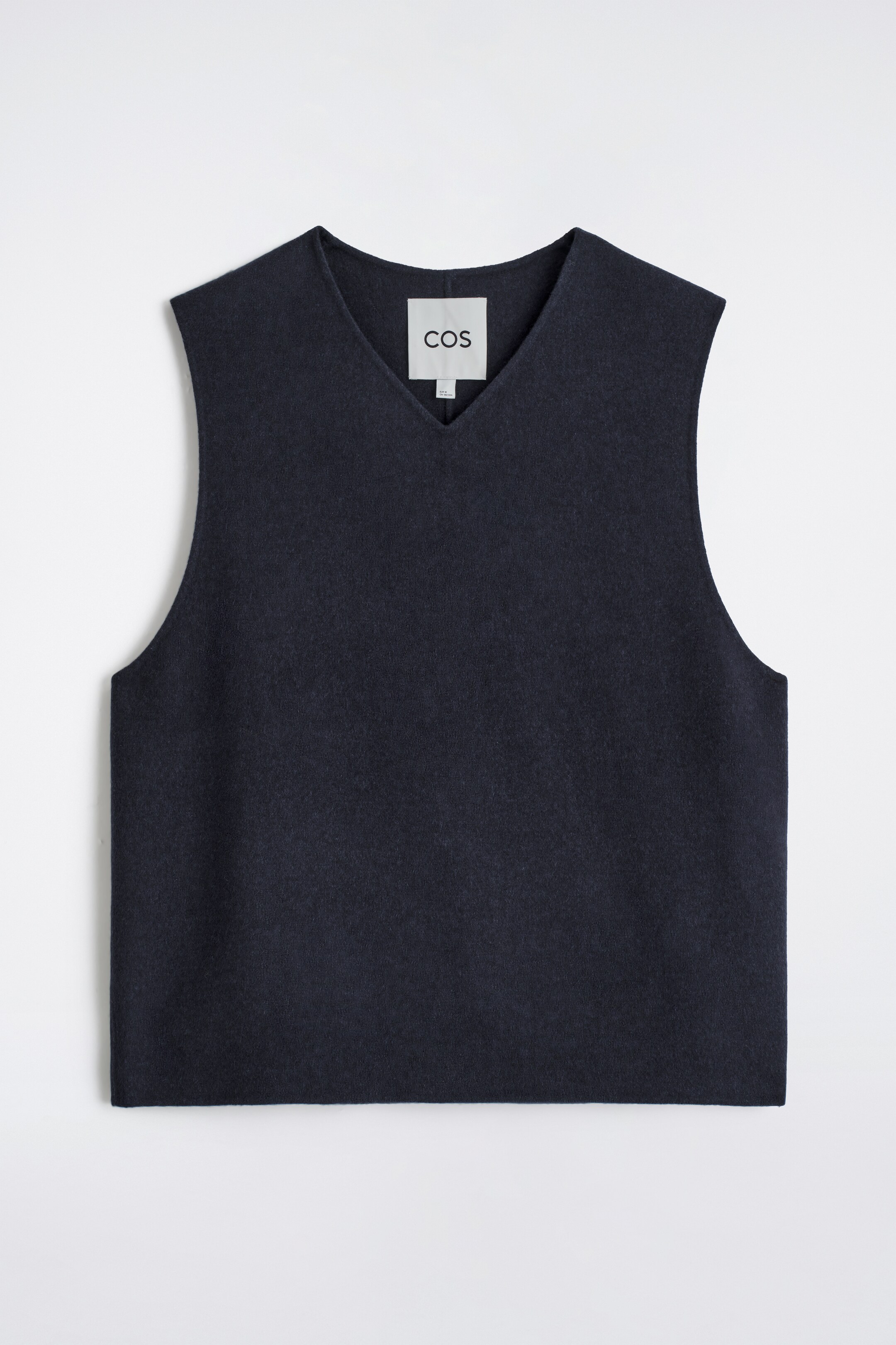 Agrandir l'image: Un gilet bleu marine à col en V est présenté de face, avec une silhouette décontractée et sans manches, et une texture lisse et mate. Une étiquette blanche de la marque COS est visible à l'intérieur du col en V.