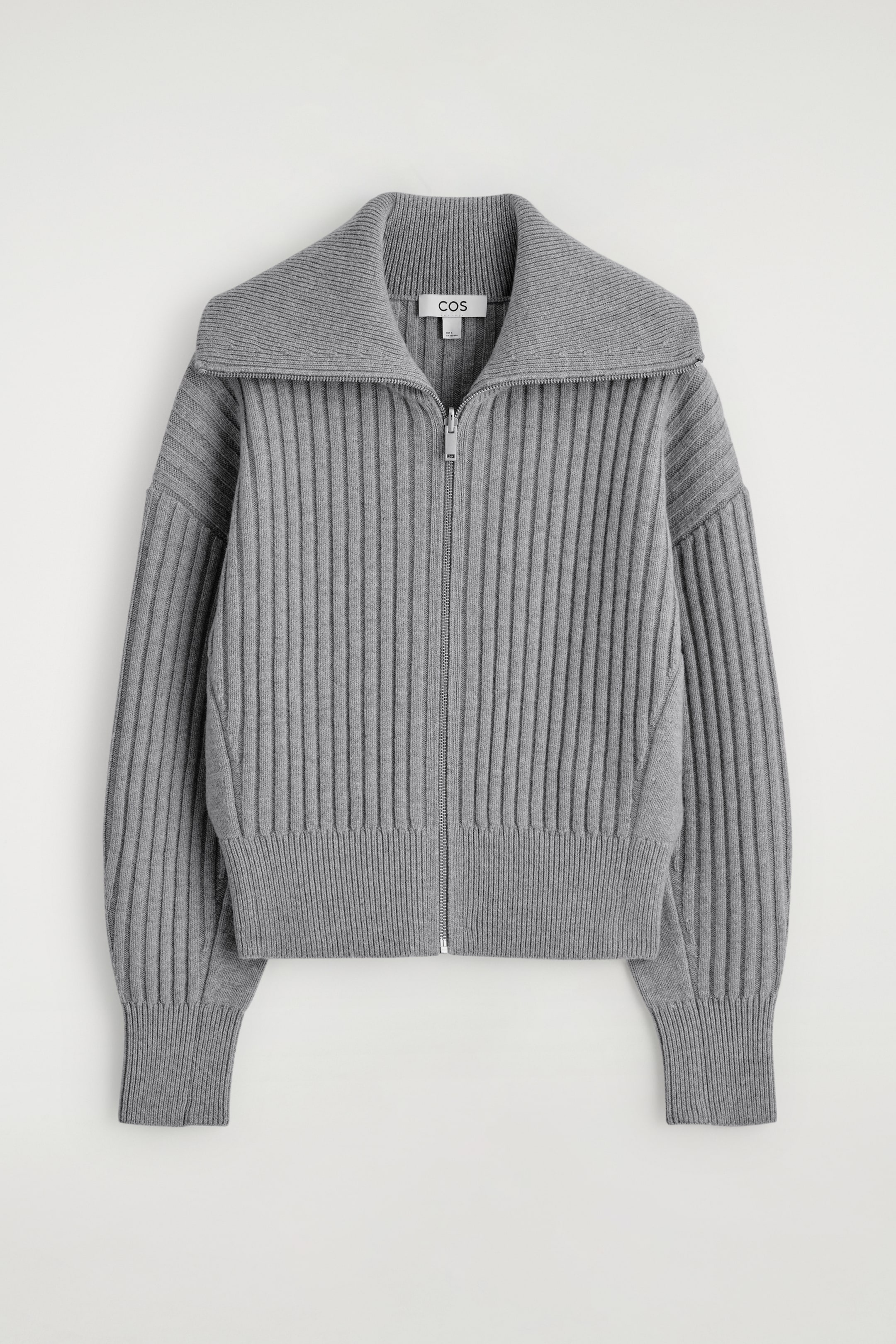 Größeres Bild ansehen: Eine graue gerippte Strickjacke wird von vorne präsentiert, mit einem breiten, gespreizten Kragen und einem durchgehenden silberfarbenen Reißverschluss. Der Körper und die langen Ärmel zeigen ein markantes vertikales Rippmuster, das mit gerippten Bündchen und einem gerippten Saum abschließt.