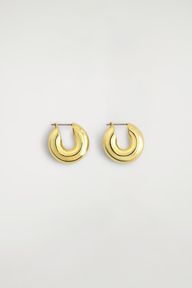 Mini chunky hoop earrings are displayed in a thick, rounded C-shape design with a highly polished gold-toned finish. The earrings are shown front-on, showcasing their curved, tubular structure and straight post-back fastenings. - 1