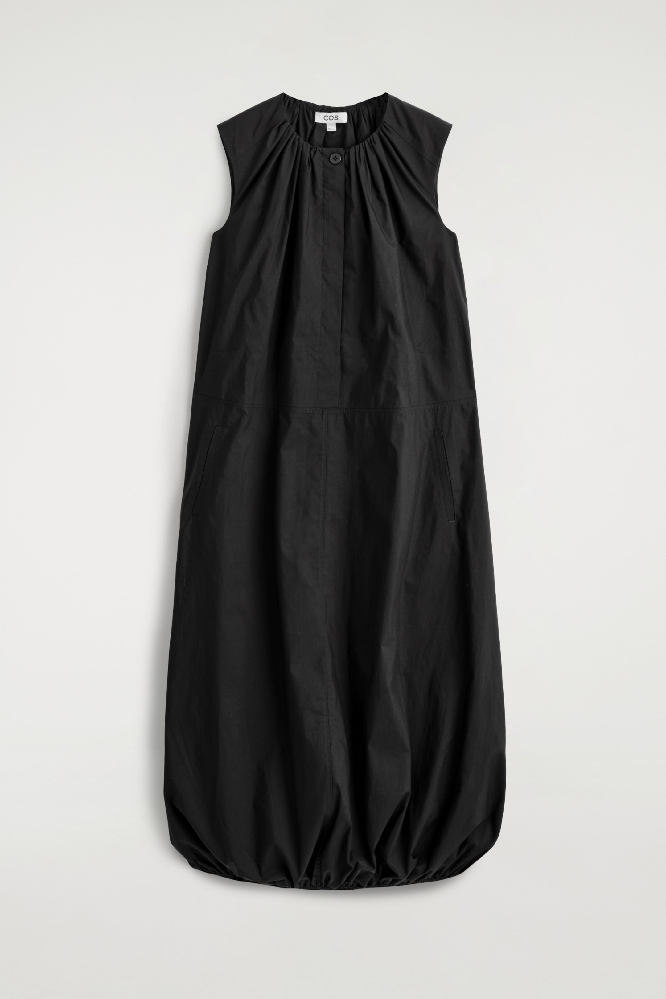Agrandir l'image: Une robe midi noire est présentée à plat, face à l'avant, mettant en valeur une coupe décontractée et un col rond froncé avec des manches courtes de type cap. Elle présente un seul bouton visible en haut d'une patte de boutonnage cachée à l'avant, des poches fendues verticales discrètes sur les côtés, et un ourlet bouffant froncé.