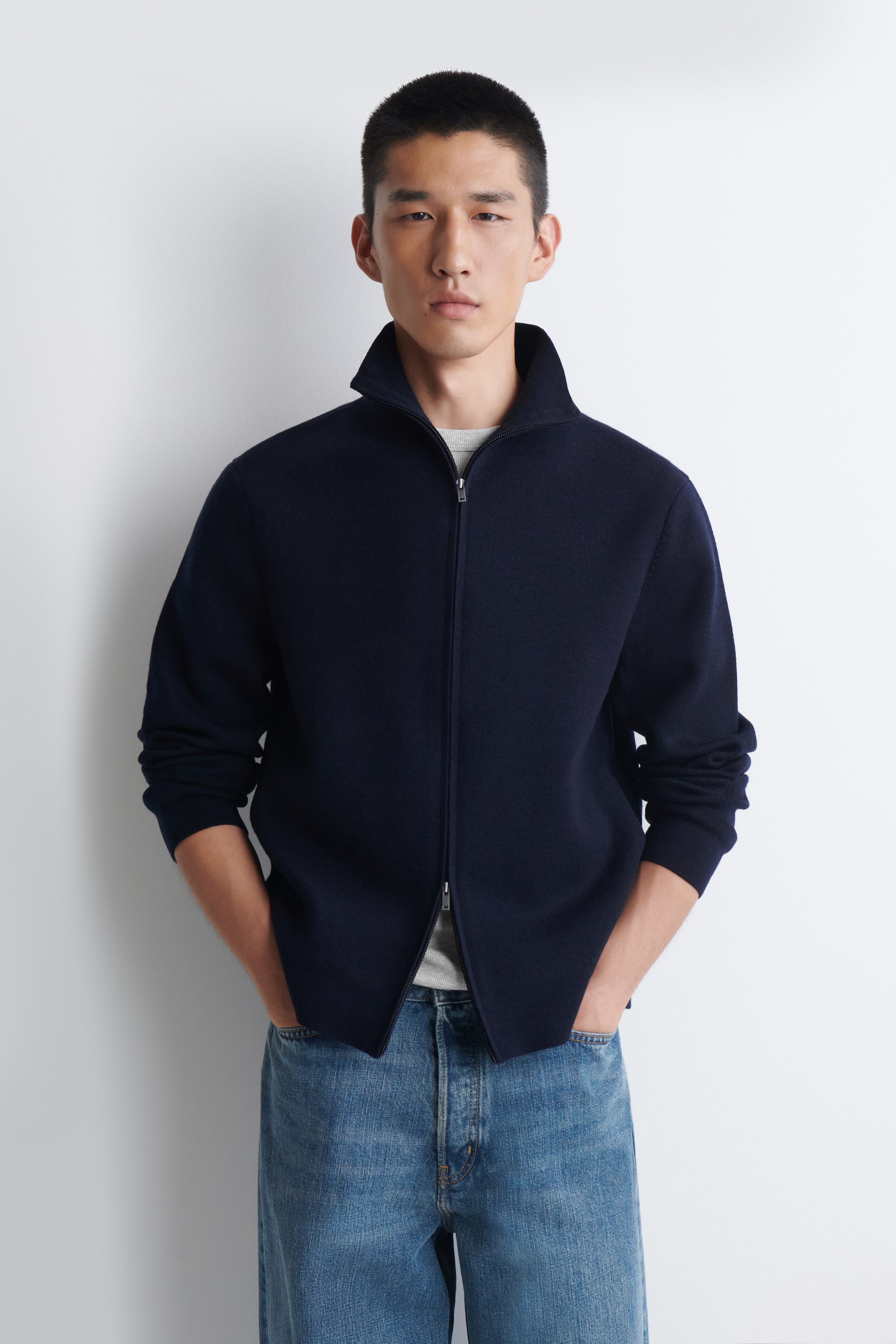 View larger image: This navy Milano-knit jacket is presented from the front, showcasing a stand-up funnel neck and a silver-toned double-ended zip running down the centre front. The zip is partially undone from the bottom, revealing a light grey T-shirt underneath, and the jacket has a regular fit with long sleeves.