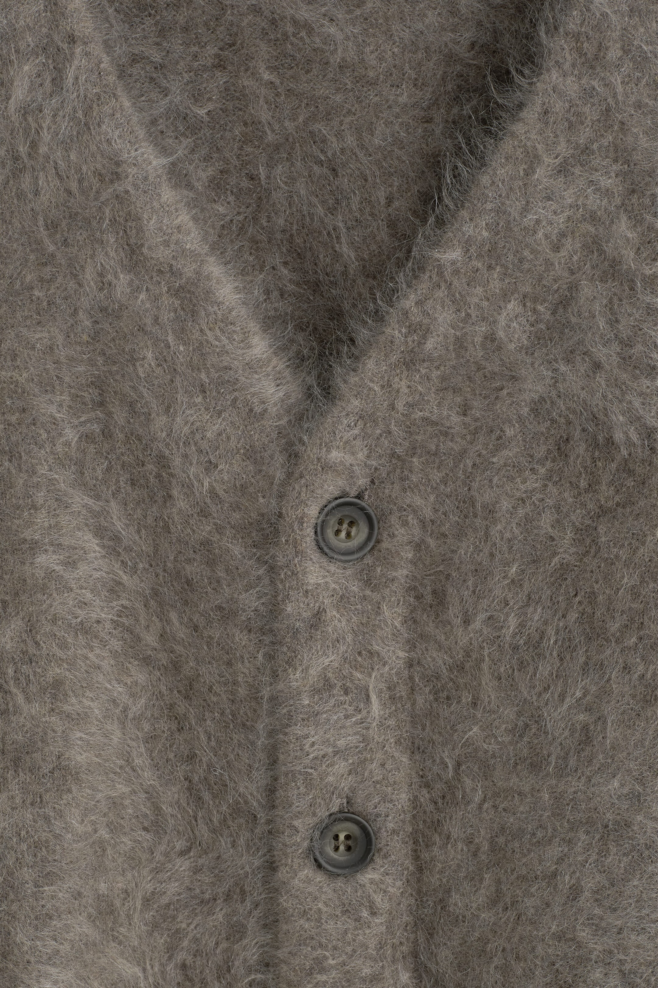 Le cardigan à col en V en cachemire brossé présente, en gros plan de face, sa surface gris-brun très texturée et duveteuse. Deux boutons gris foncé ferment la patte de boutonnage centrale sous l’encolure en V. Le cardigan à col en V en cachemire brossé présente, en gros plan de face, sa surface gris-brun très texturée et duveteuse. Deux boutons gris foncé ferment la patte de boutonnage centrale sous l’encolure en V.