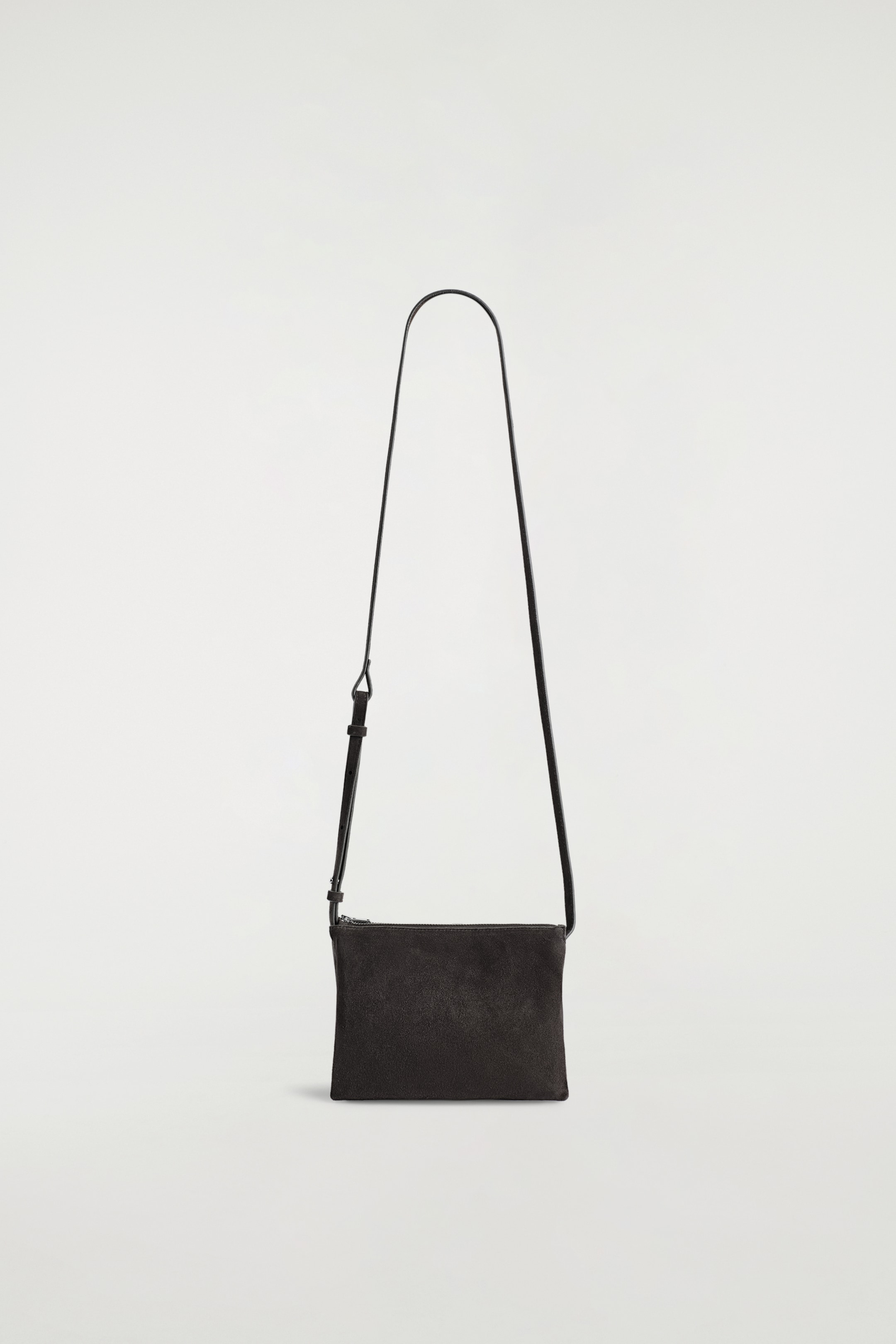 Agrandir l'image: Un sac bandoulière en daim rectangulaire et sombre est suspendu verticalement, affichant son devant. Il est doté d'une fine sangle noire réglable et d'une fermeture éclair sur le dessus.
