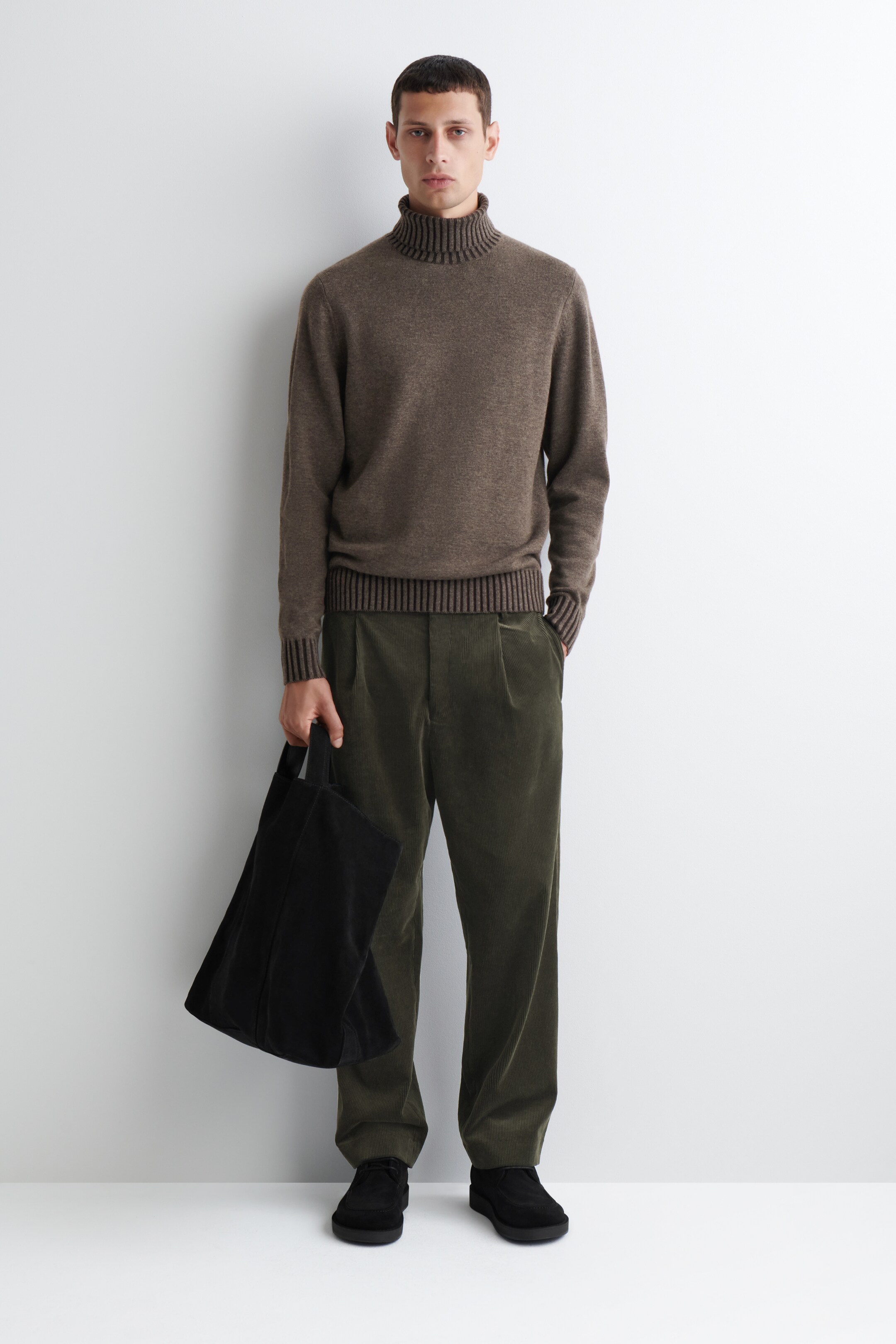 View larger image: A brown textured knit turtleneck sweater, featuring a ribbed collar, cuffs, and hem, is being presented. It is styled with olive green wide-wale corduroy pants, cut with a relaxed fit and front pleats, and black low-cut shoes; a black tote bag is also being carried.