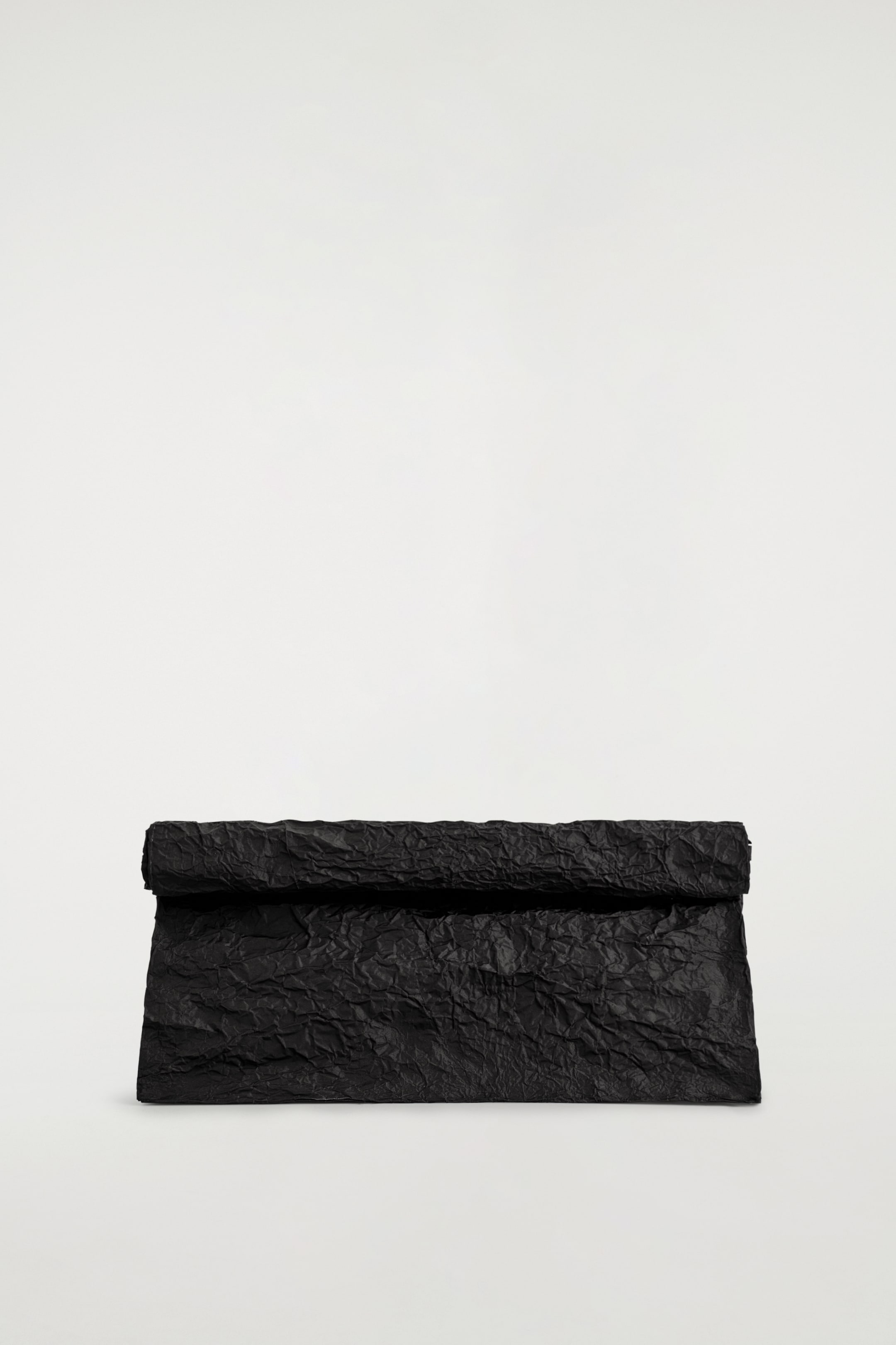 Visualizza immagine più grande: Una borsa a mano nera è appoggiata piatta, presentata dalla parte anteriore. È caratterizzata da una silhouette rettangolare oversize con il bordo superiore arrotolato per chiudere, e il suo tessuto appare stropicciato e strutturato.