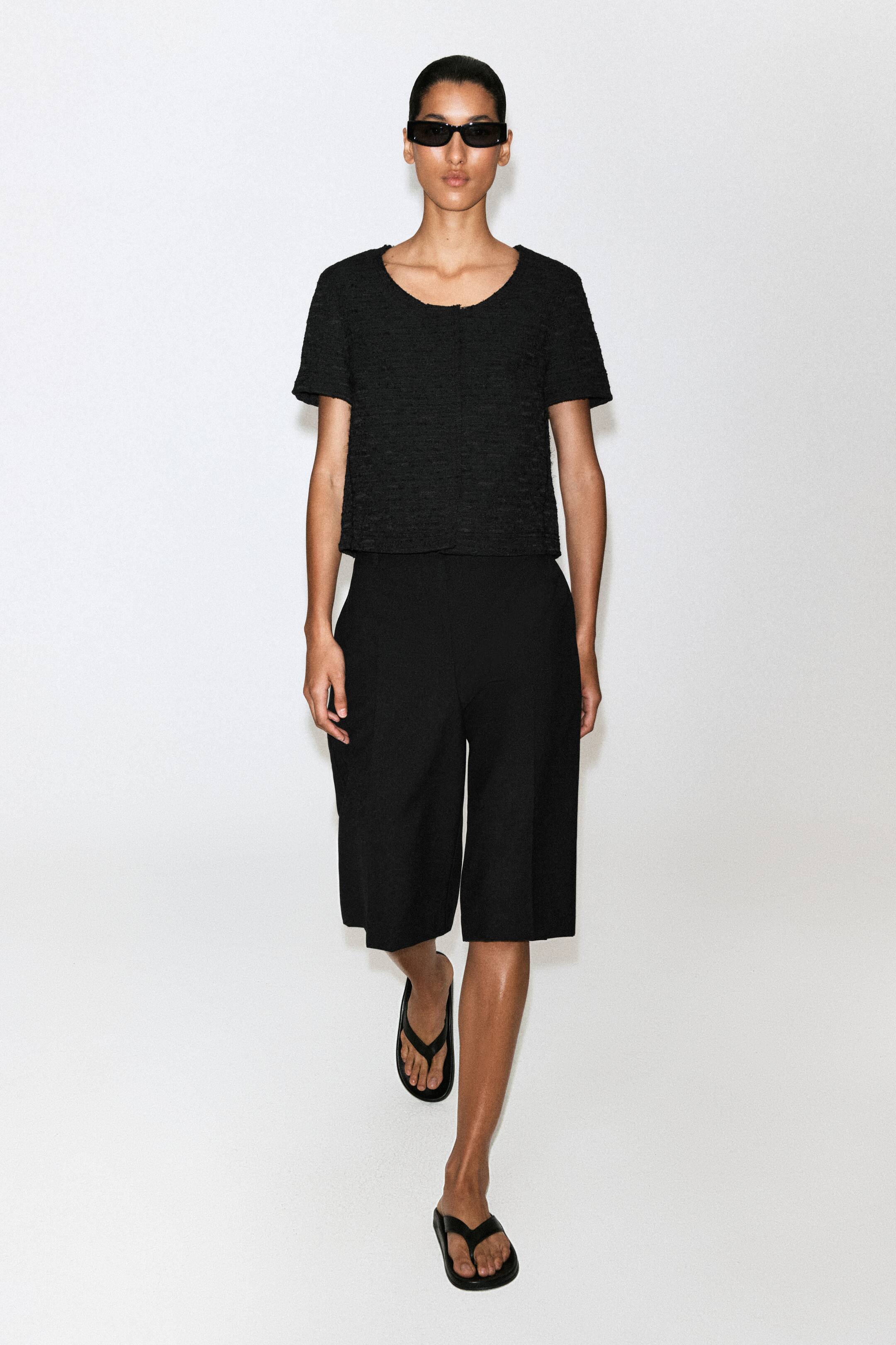 Visualizza l'immagine ingrandita: Gli shorts Bermuda neri su misura sono mostrati frontalmente, con una silhouette rilassata a gamba ampia e pieghe stirate strutturate che scendono al centro di ciascuna gamba. Gli shorts arrivano al ginocchio e presentano un design pulito e minimalista.