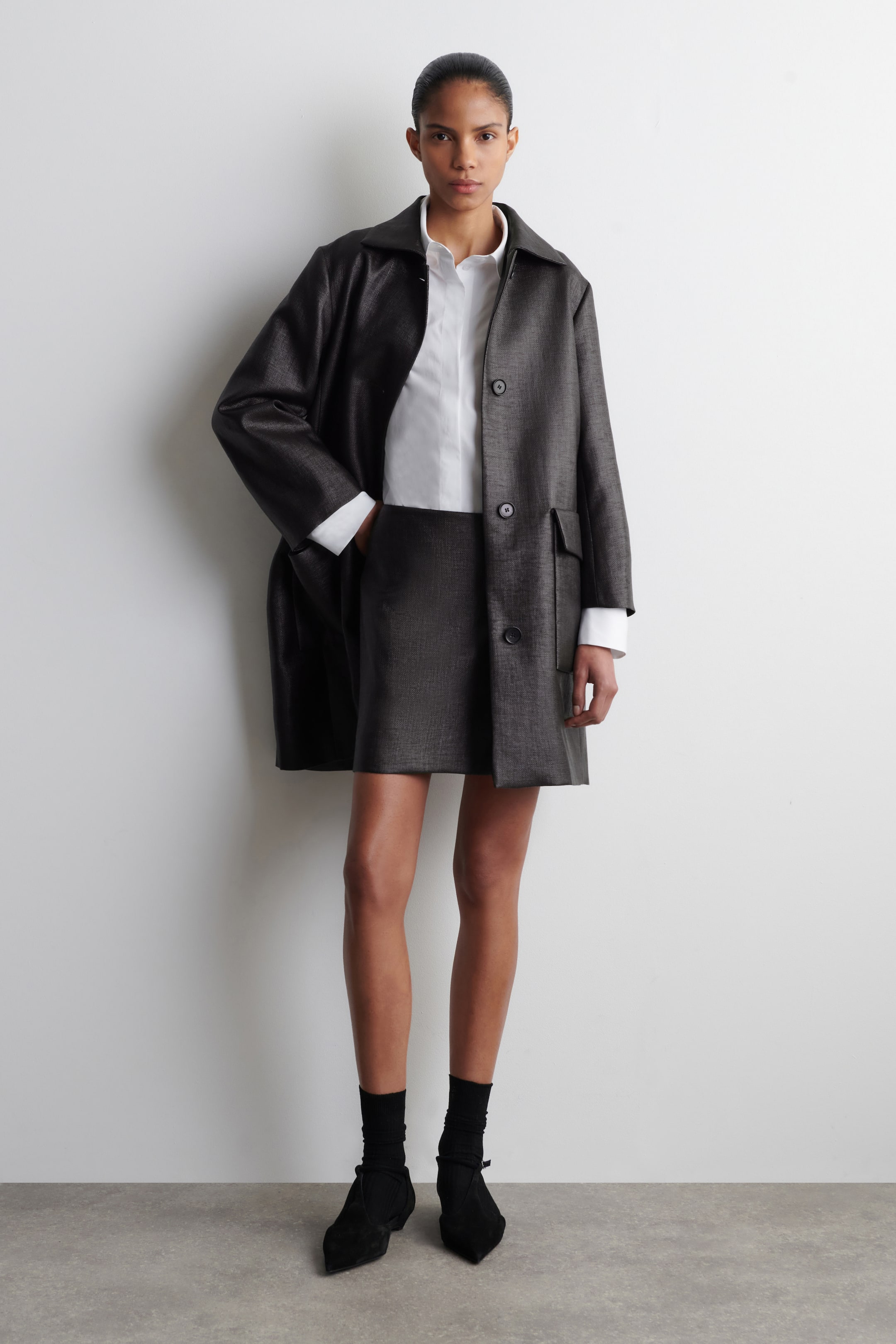 הצגת תמונה גדולה יותר: החלק הקדמי של החצאית המיני הזו מציג גזרה רגילה בגוון גרפיט עם ברק עדין. היא כוללת משטח מרקם וחיצים מעוצבים במותן.