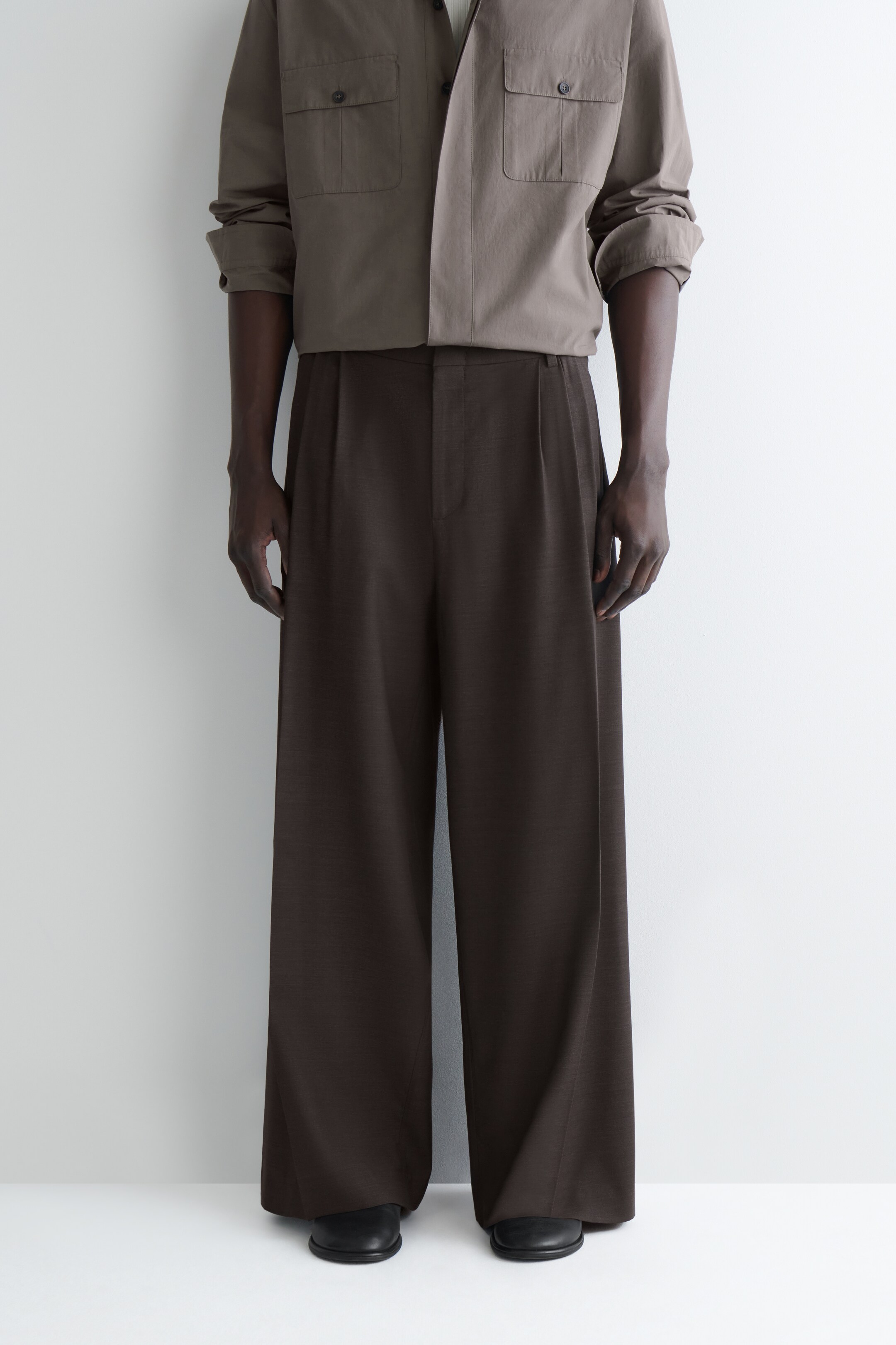 Größeres Bild ansehen: Dunkelbraune Hosen mit weitem Bein werden von vorne präsentiert, mit Falten an der Taille und einem Schnitt in voller Länge, der über die Schuhe fällt.