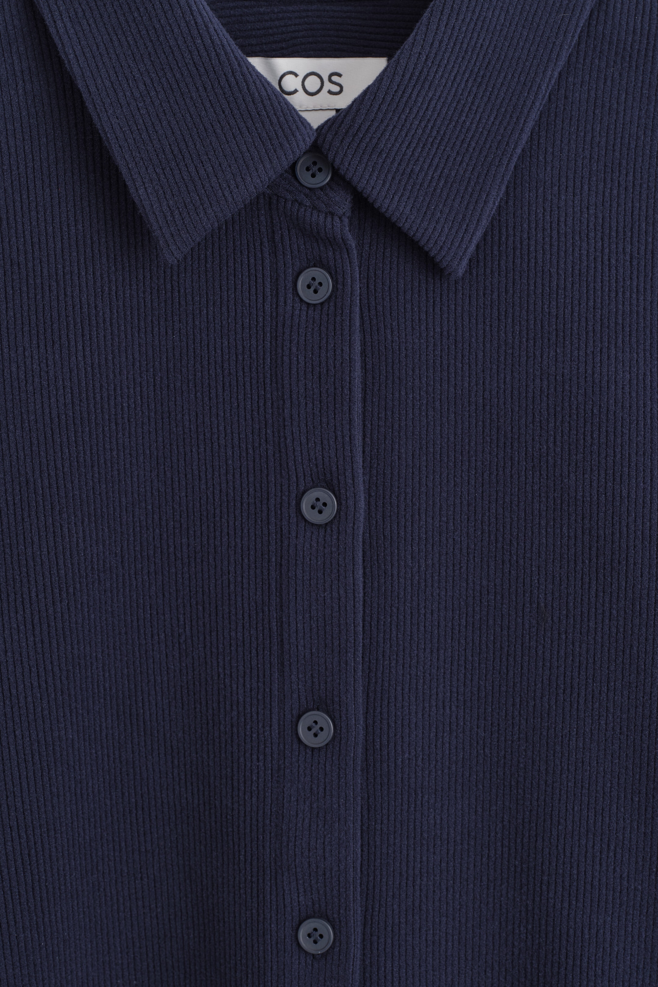 This corduroy jersey shirt shows a close-up front view of its dark navy blue ribbed fabric. It features a classic pointed collar and a button-down placket with matching dark buttons. This corduroy jersey shirt shows a close-up front view of its dark navy blue ribbed fabric. It features a classic pointed collar and a button-down placket with matching dark buttons.