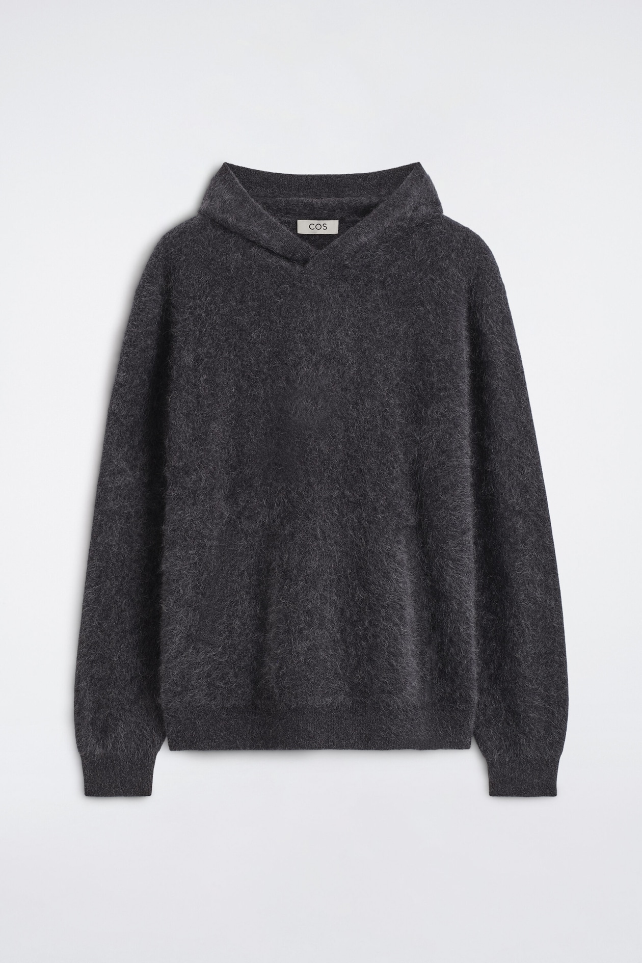A brushed pure cashmere hoodie in dark gray is shown from the front, showcasing its soft, fuzzy texture and relaxed hood. The garment features long sleeves with ribbed cuffs and a matching ribbed hem.