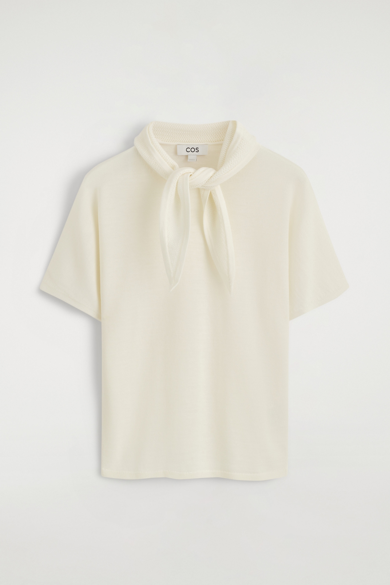 The scarf-detail merino wool-blend T-shirt is shown from the front, highlighting its cream-colored fine-knit design with short sleeves. It features an integrated matching scarf detail at the collar, tied in a loose knot at the chest.