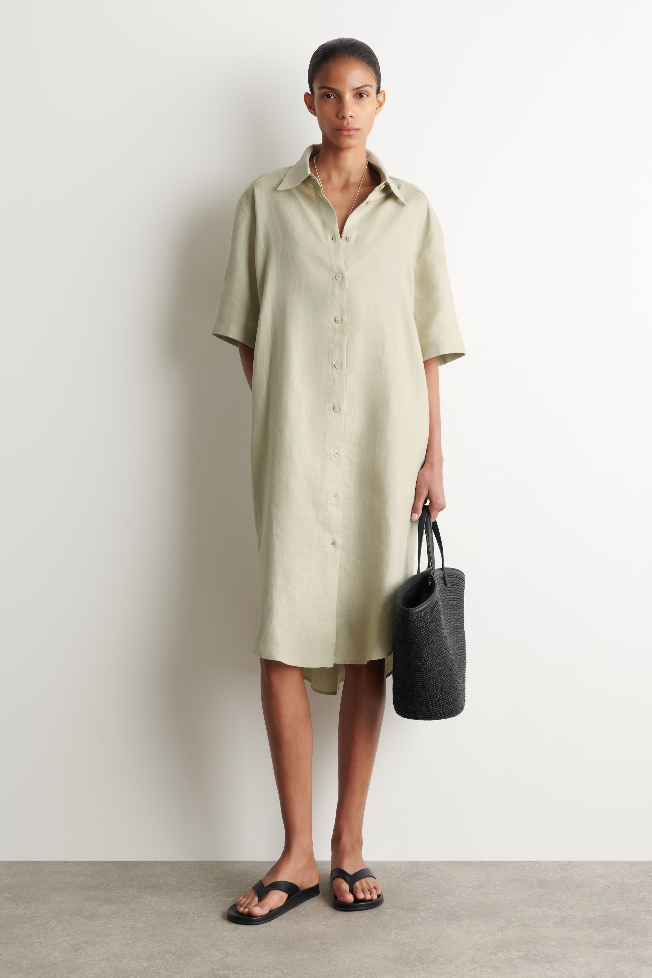 Ver imagem maior: Um vestido-camisa verde claro apresenta um corte solto e descontraído visto de frente, com uma gola em bico, mangas curtas, uma carcela de botões completa na frente e um comprimento midi.