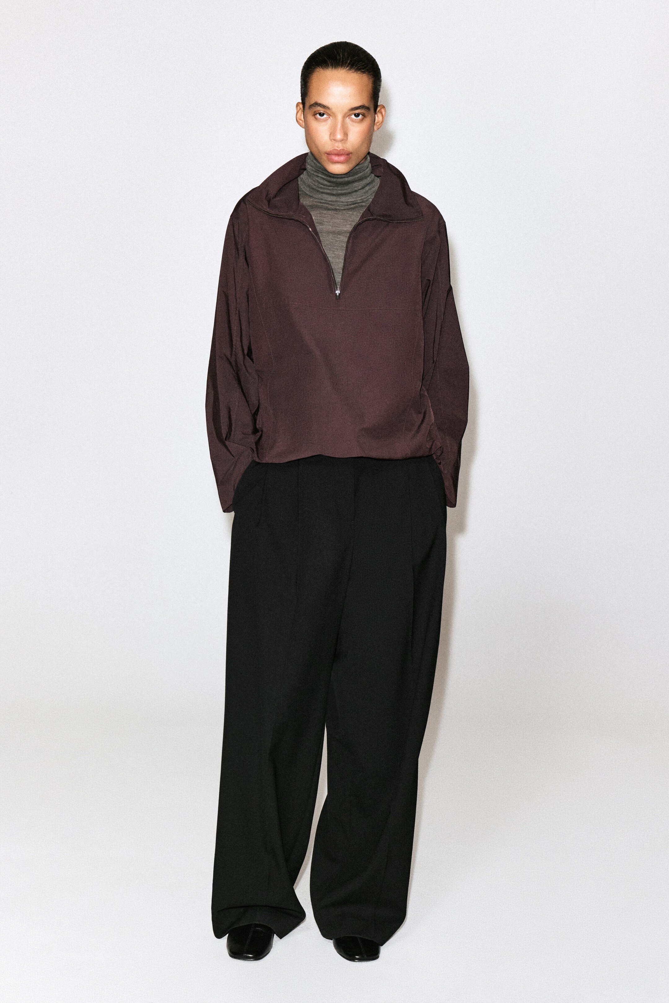This dark plum half-zip shirt is shown from the front, featuring a silver-tone zipper, a wide collar, and a relaxed silhouette. It is layered over a grey knit turtleneck and paired with black wide-leg trousers. This dark plum half-zip shirt is shown from the front, featuring a silver-tone zipper, a wide collar, and a relaxed silhouette. It is layered over a grey knit turtleneck and paired with black wide-leg trousers.