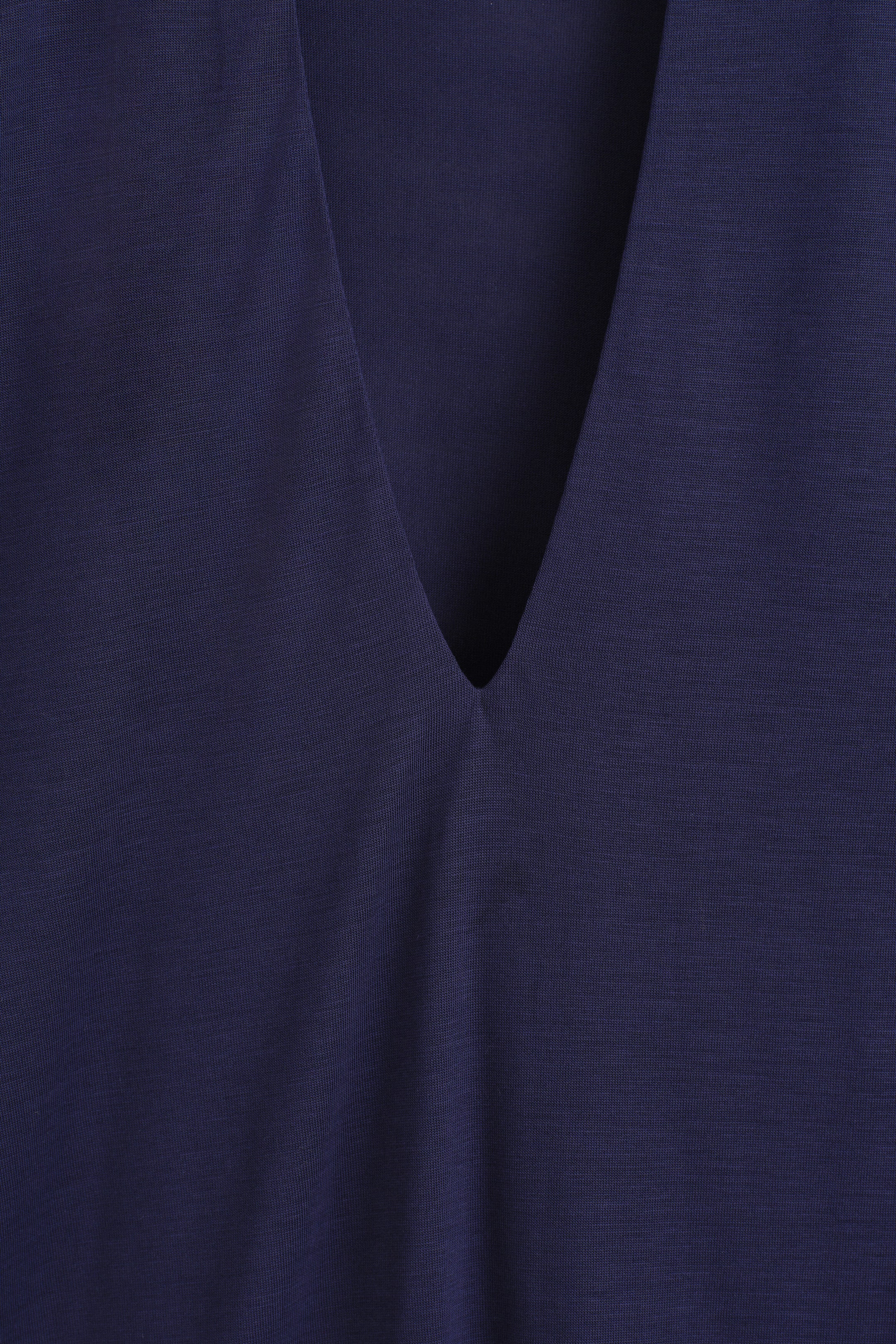 A close-up view of the front of a navy blue jersey top shows a deep V-neckline with clean-cut edges and subtle gathering at the base. A close-up view of the front of a navy blue jersey top shows a deep V-neckline with clean-cut edges and subtle gathering at the base.