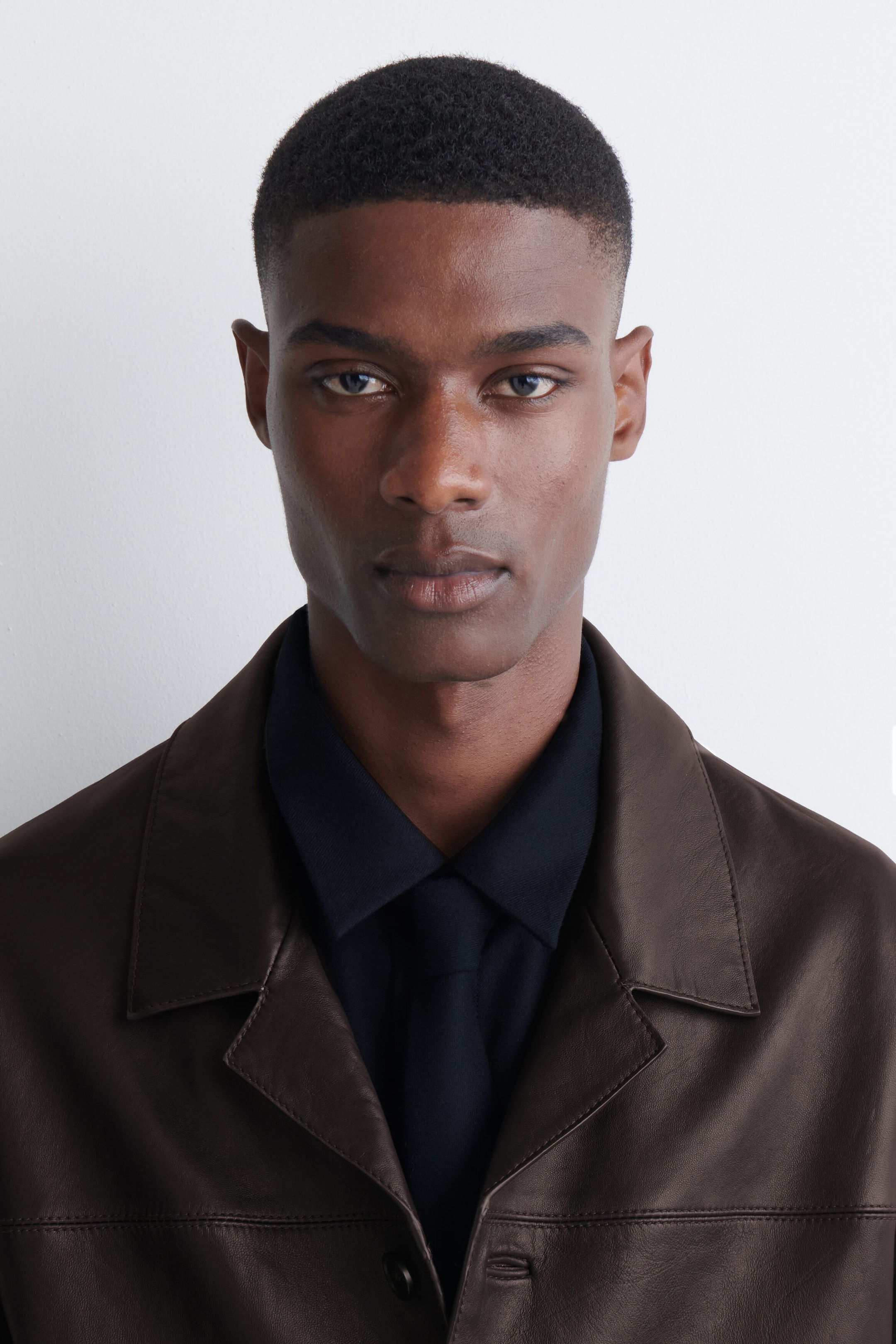 The model is wearing a dark navy wool flannel tie, knotted beneath a matching collared shirt. The shirt and tie are layered under a dark brown leather jacket. The model is wearing a dark navy wool flannel tie, knotted beneath a matching collared shirt. The shirt and tie are layered under a dark brown leather jacket.
