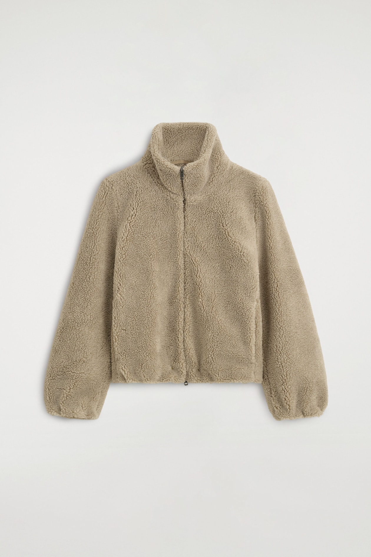 A beige funnel-neck teddy jacket is shown from the front, featuring a highly textured sherpa fleece fabric and a full-length centre zipper. The jacket displays a high stand collar, long sleeves with gathered cuffs, and a slightly elasticized hem.