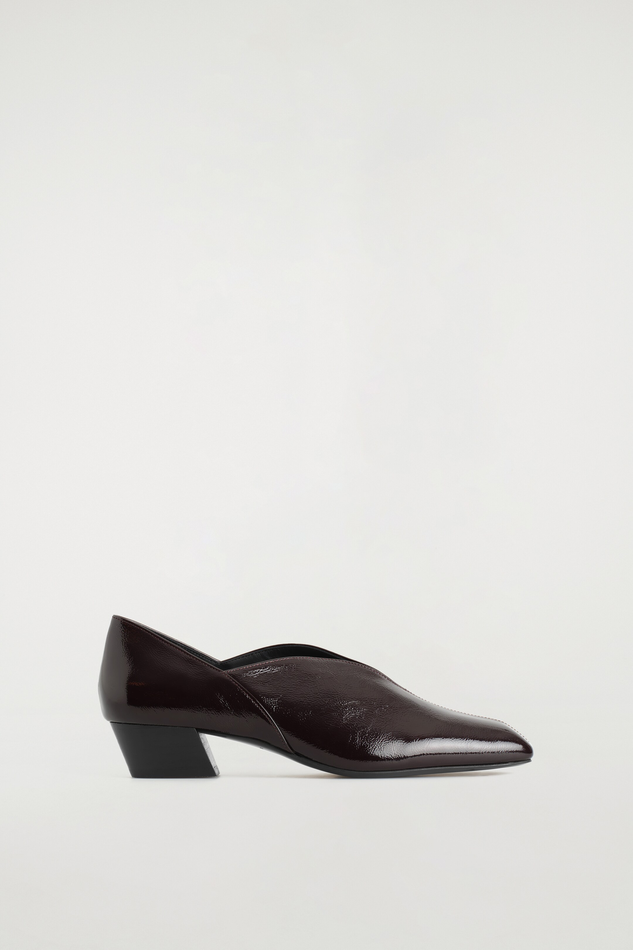 Agrandir l'image: Orientée vers la droite, une ballerine moderne de couleur bordeaux, confectionnée en cuir verni, présente une silhouette angulaire avec un décolleté en V, des bouts carrés, et repose sur un petit talon bloc noir.