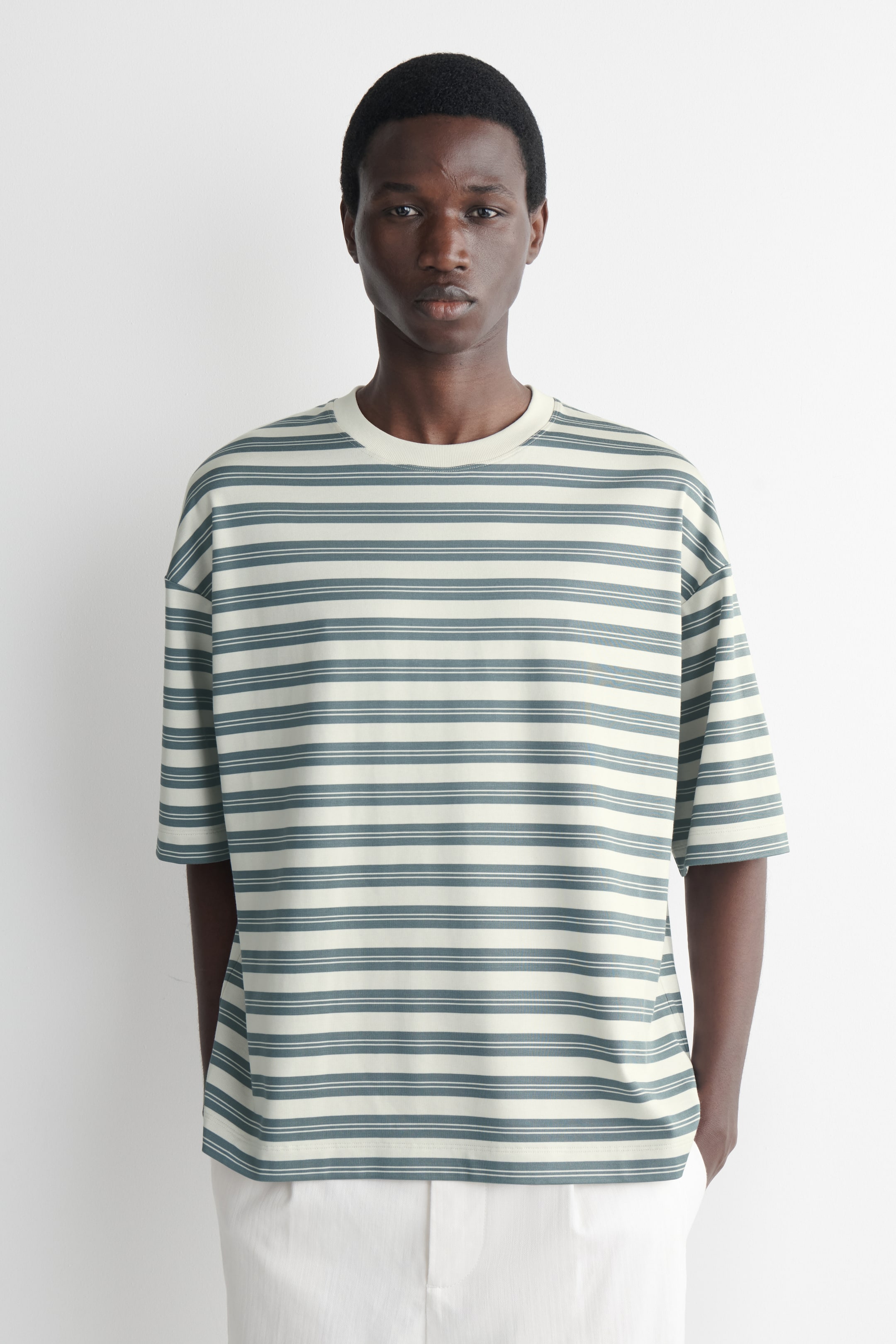 Agrandir l'image: Un t-shirt crème avec des rayures horizontales variées en bleu sarcelle et crème est présenté, face avant. Il est doté d'un col rond côtelé et de manches courtes à coupe décontractée.