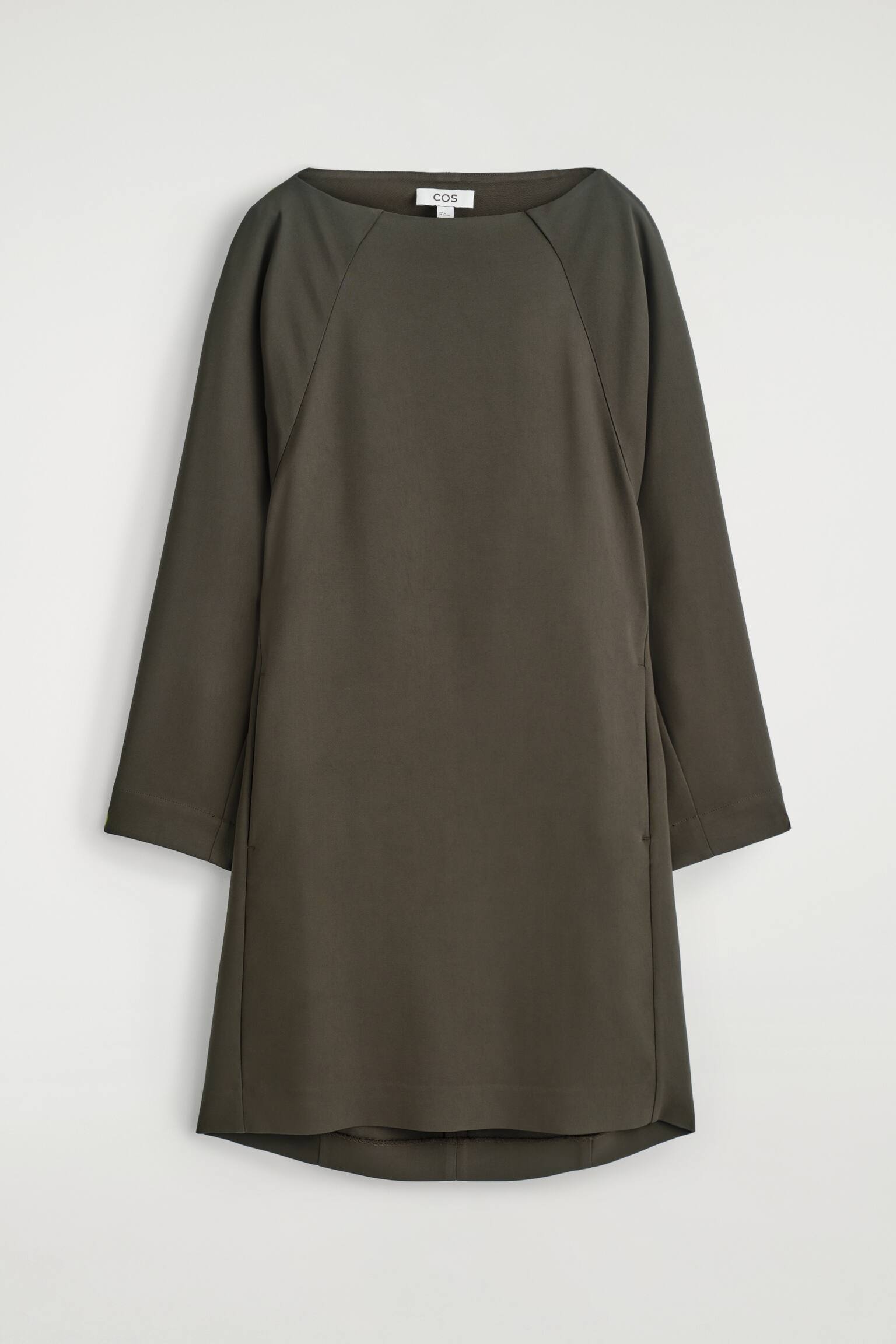 Un vestido verde oliva oscuro presenta un escote barco y mangas raglán largas. El vestido de corte recto y suelto termina por encima de la rodilla y está detallado con dos pequeños botones circulares en el lado inferior izquierdo.