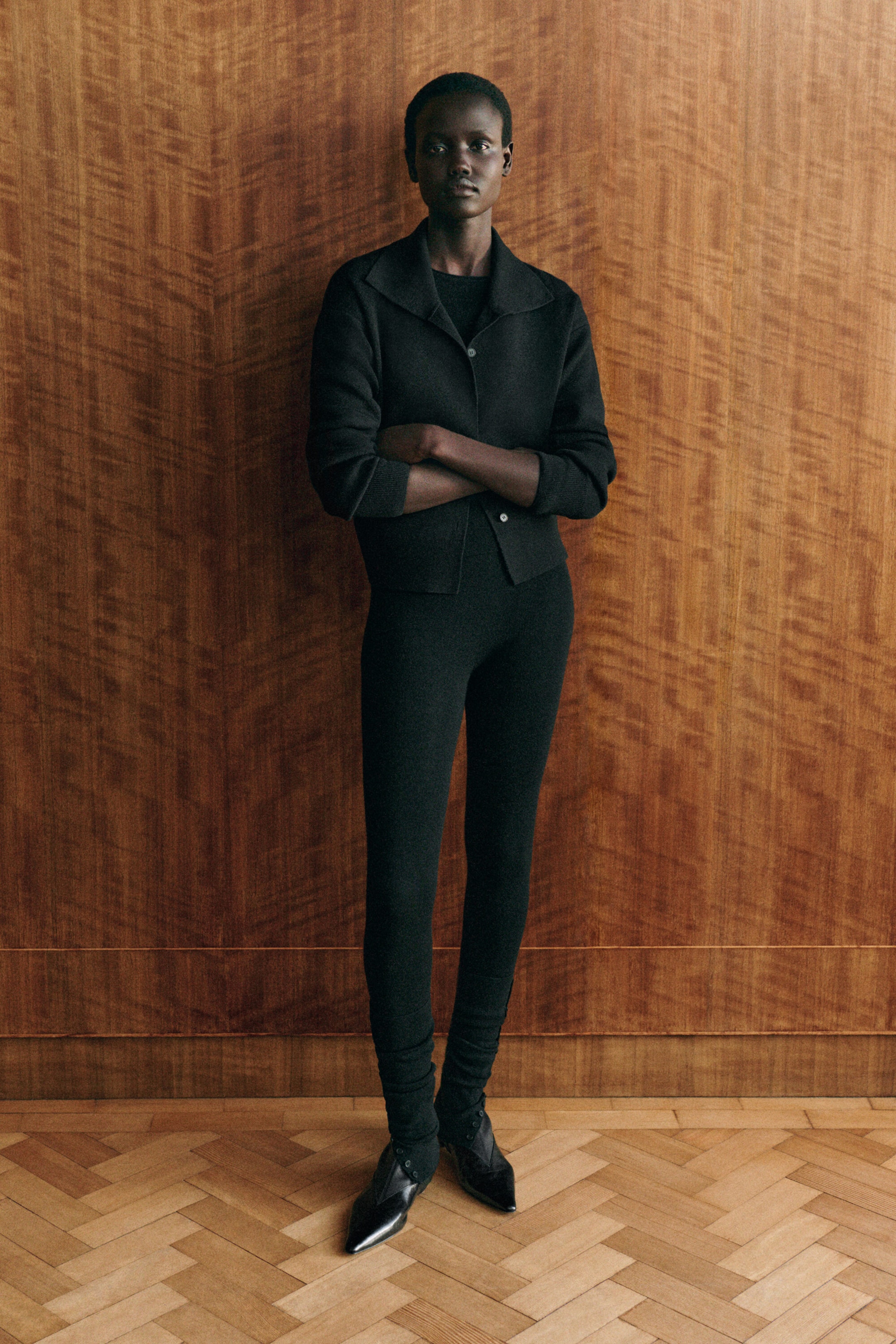 Un mannequin fait face à l’avant et porte un cardigan à col montant en laine mérinos noire avec fermeture à boutons et poignets côtelés, superposé à un haut noir assorti. Le cardigan est agencé avec des leggings sans couture en laine mérinos noire assortis, à coupe ajustée et avec détails froncés et côtelés aux chevilles. Un mannequin fait face à l’avant et porte un cardigan à col montant en laine mérinos noire avec fermeture à boutons et poignets côtelés, superposé à un haut noir assorti. Le cardigan est agencé avec des leggings sans couture en laine mérinos noire assortis, à coupe ajustée et avec détails froncés et côtelés aux chevilles.