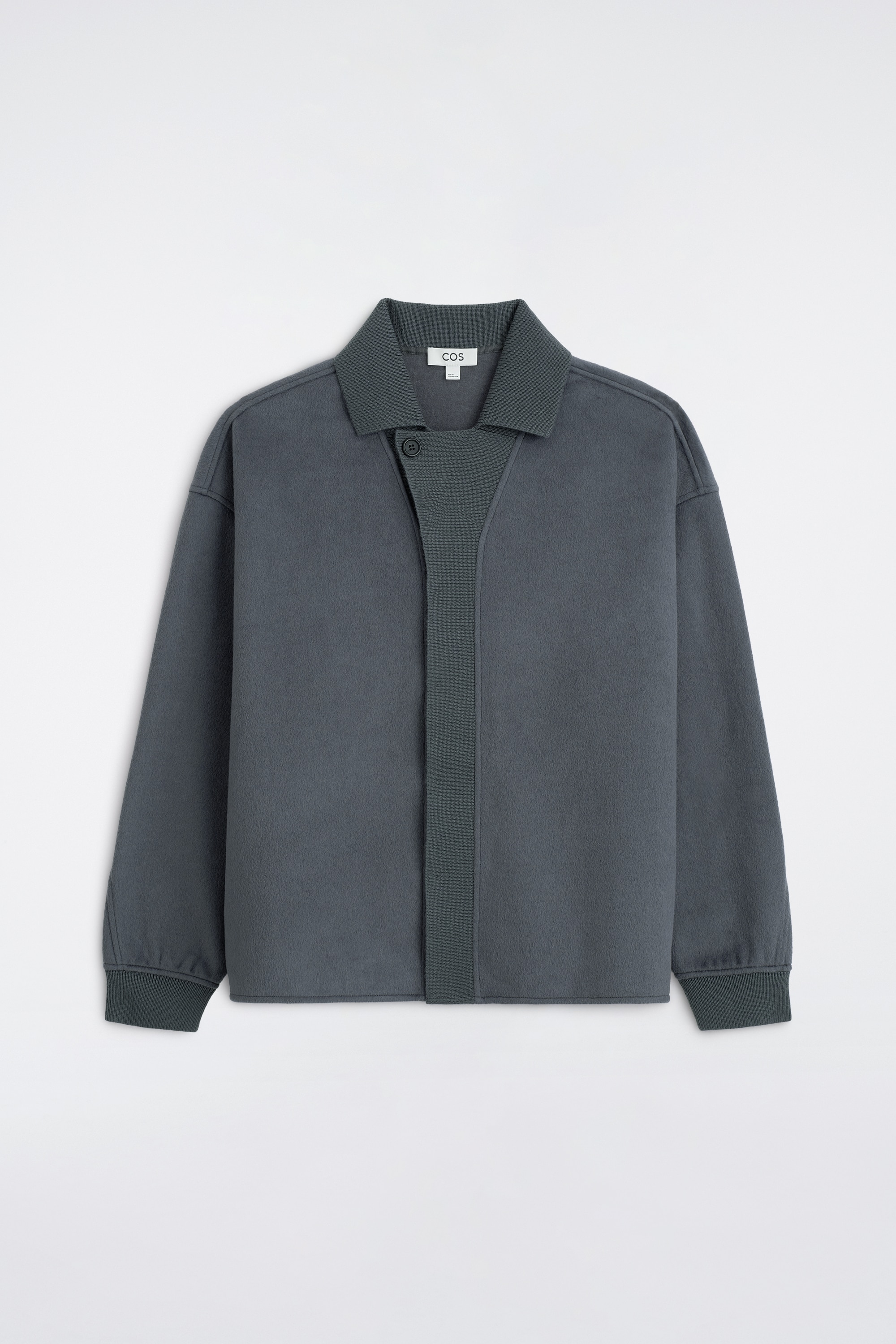 Das Model trÃ¤gt eine dunkelgraue Strickjacke mit Kragen und eine dazu passende weit geschnittene Hose. Die offene Jacke ist Ã¼ber einem hellgrauen Hemd mit Knopfleiste und einem weiÃen T-Shirt getragen und mit schwarzen Leder-Loafers kombiniert.